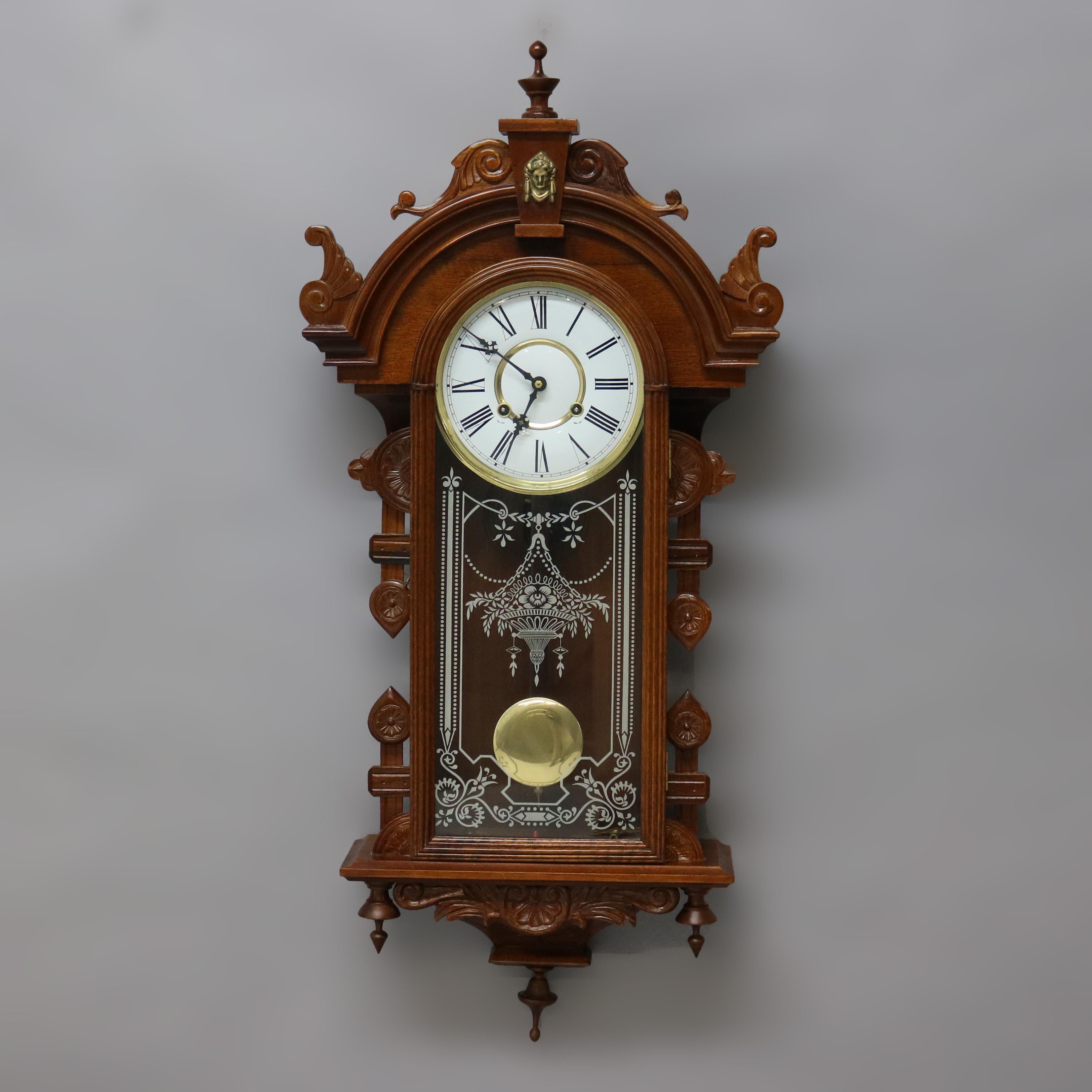 A Victorian style wall clock offers mahogany case with arched crest having scroll work and finials with central female mask over case with glass door, scrolls and finials throughout, 20th century

Measures- 38.25''H x 18.25''W x 5.5''D.