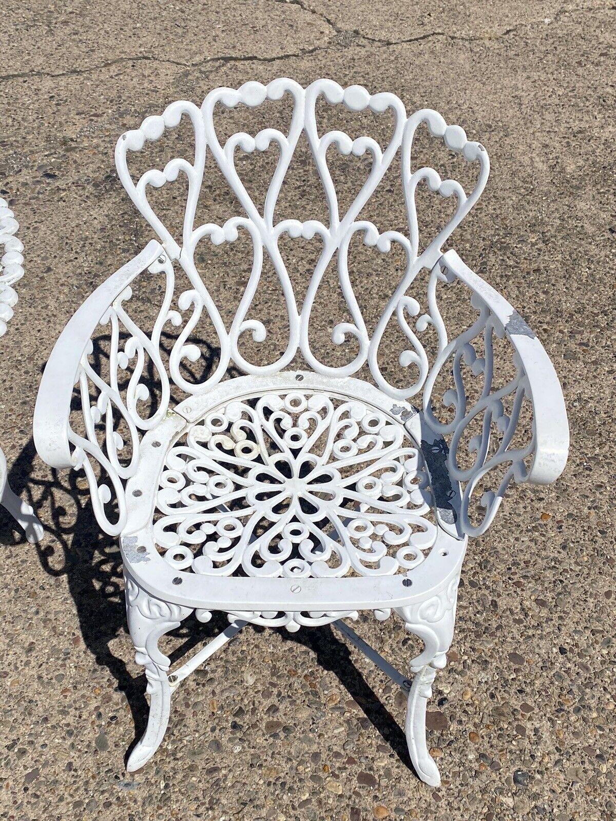 Victorian Style Cast Aluminum Scrolling Heart Back Garden Patio 3 Pc Bistro Set. Item features 2 heart back chairs, 1 round table with umbellar hold, scrollwork throughout, white painted finish. Circa Late 20th Century.
Measurements: 
Chairs: 31