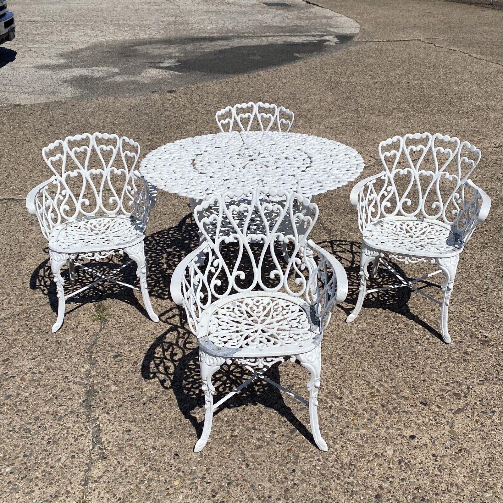 Victorian Style Cast Aluminum Scrolling Heart Back Garden Patio 3 Pc Bistro Set. Item features 4 heart back chairs, 1 round table with umbrella hold, scroll work throughout, white painted finish. Circa Late 20th Century Measurements: Chairs: 31
