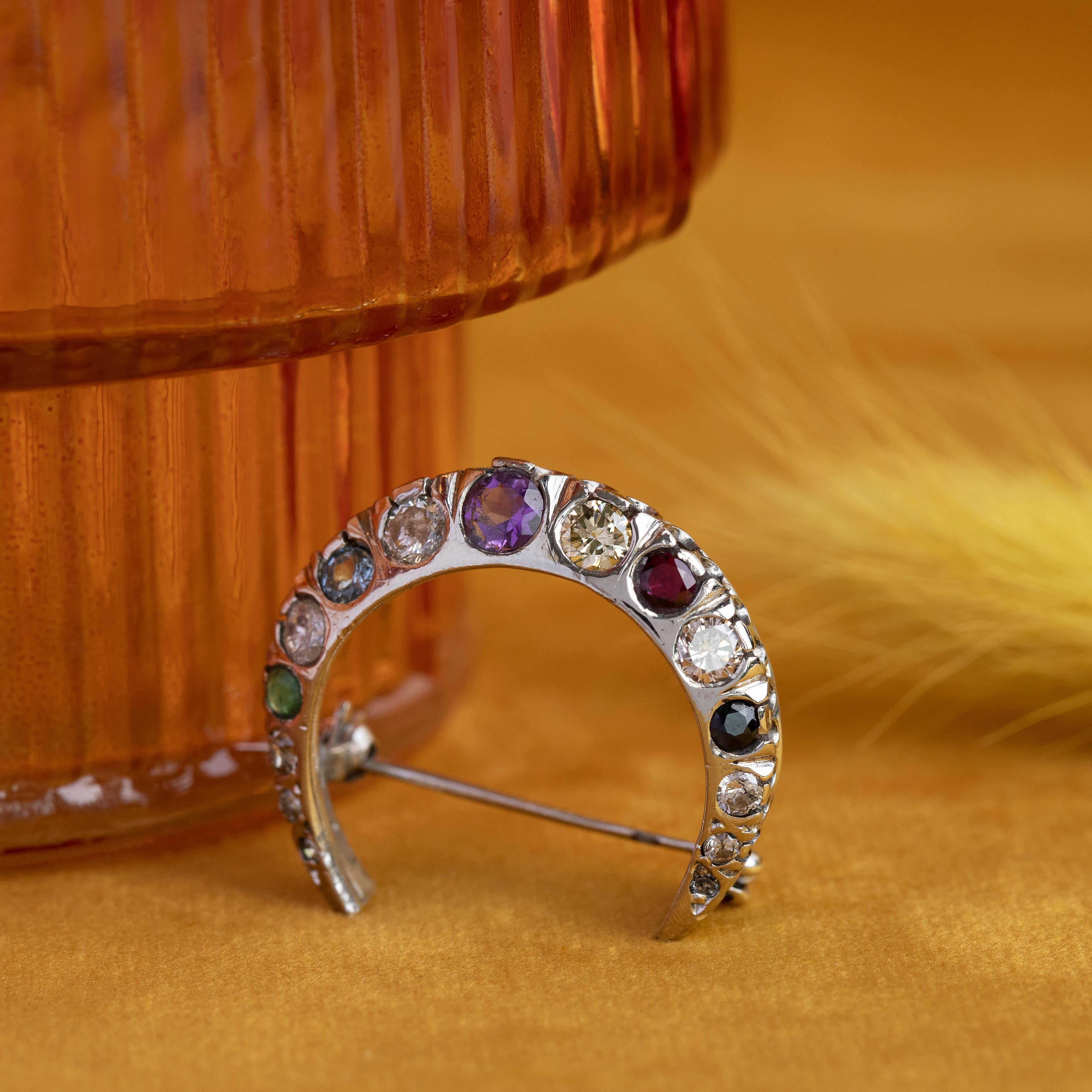 Présentant l'un des bijoux les plus sentimentaux de la collection, cette broche en forme de croissant de lune est réalisée en or blanc massif 14 carats et sertie d'un ensemble coloré de pierres précieuses en verre et de diamants. Profondément