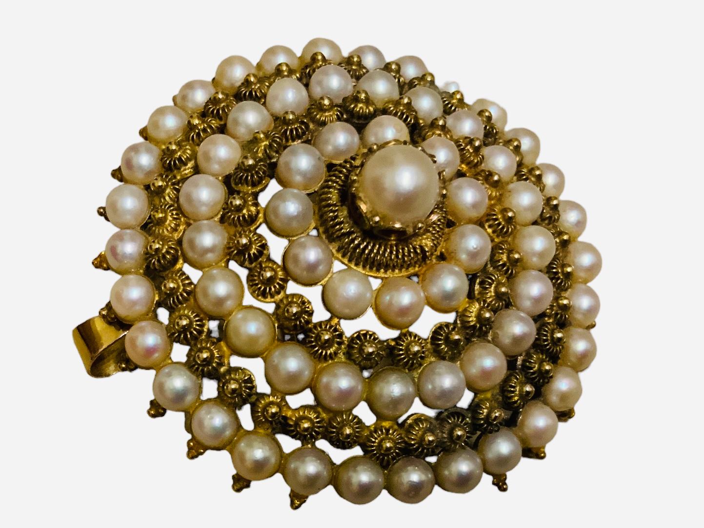 This is a Victorian style 14K yellow gold and pearls brooch/pendant. It is a round brooch decorated with smaller to larger circles made of cannetilles and pearls. The top of the brooch is crowned with a larger pearl in prong setting. The brooch has