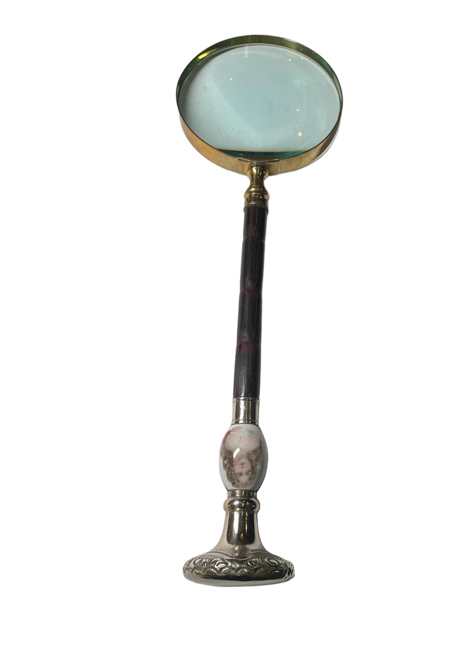 This is a round magnifying glass with long handle. The magnifying glass is enframed in gilt metal. The long handle is made of dark brown wood, but it is embellished by a hand painted portrait of a lady over an oval shaped porcelain piece. The back