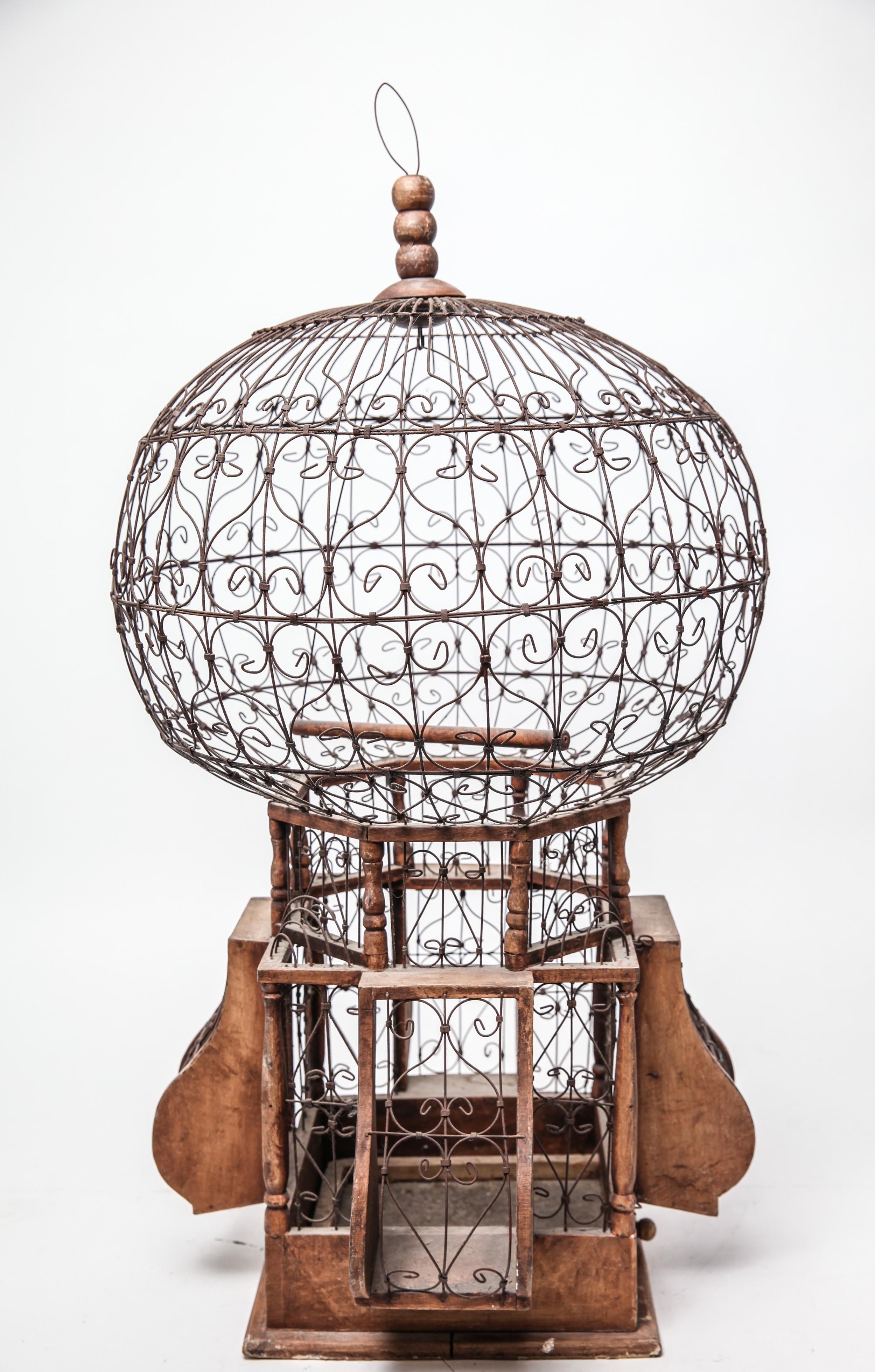 Victorian style large ornamental S-curve wire balloon form hanging bird cage on a wood and wire base, with one latching door. The piece can be pole-mounted and is in great vintage condition.