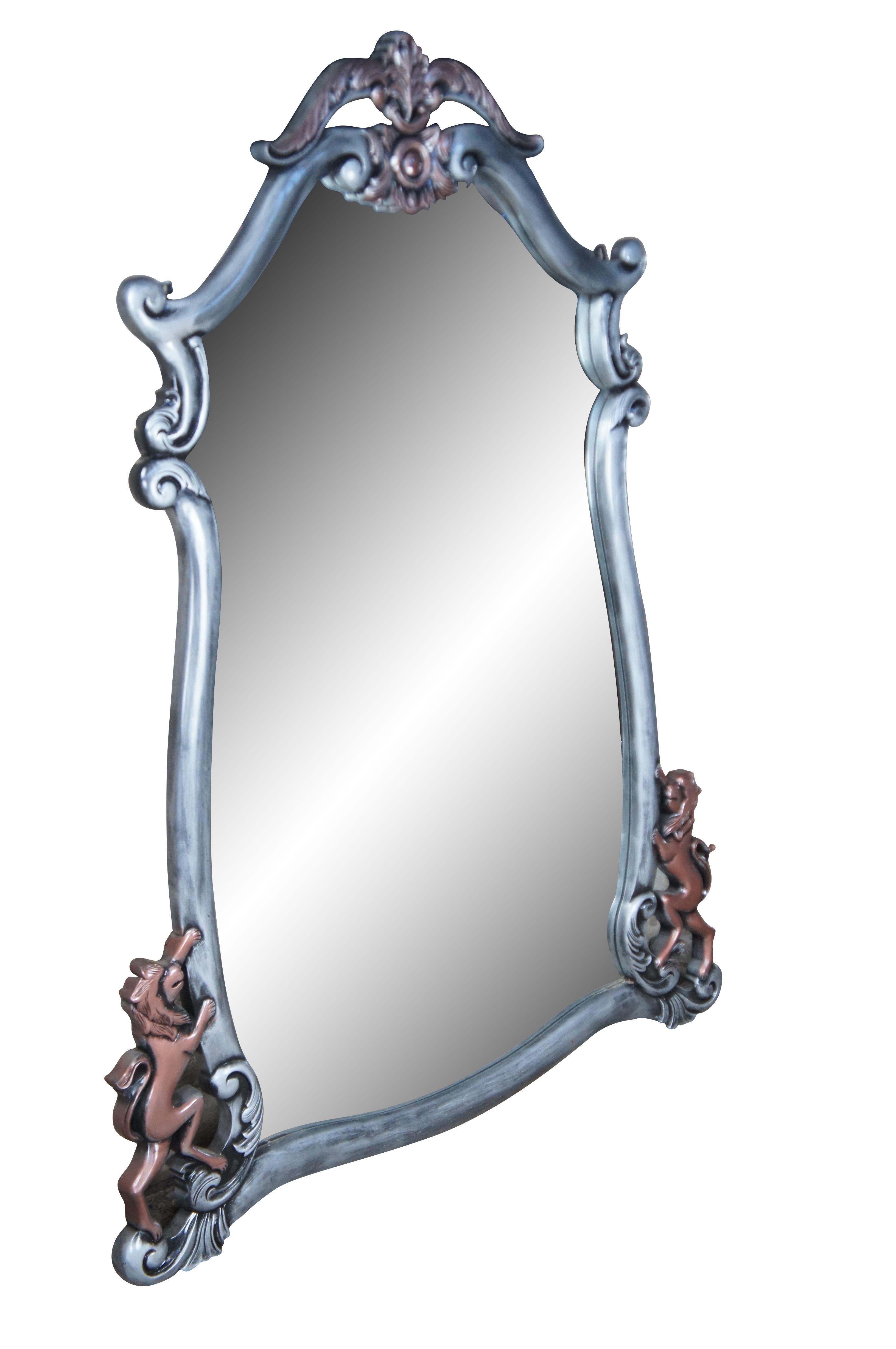 A stately Victorian Revival mirror, circa second half 20th century. Drawing inspiration from English & Irish design with figural carved lions flanked along the outside of the base. The mirror framed is made from mahogany with a silver and bronze