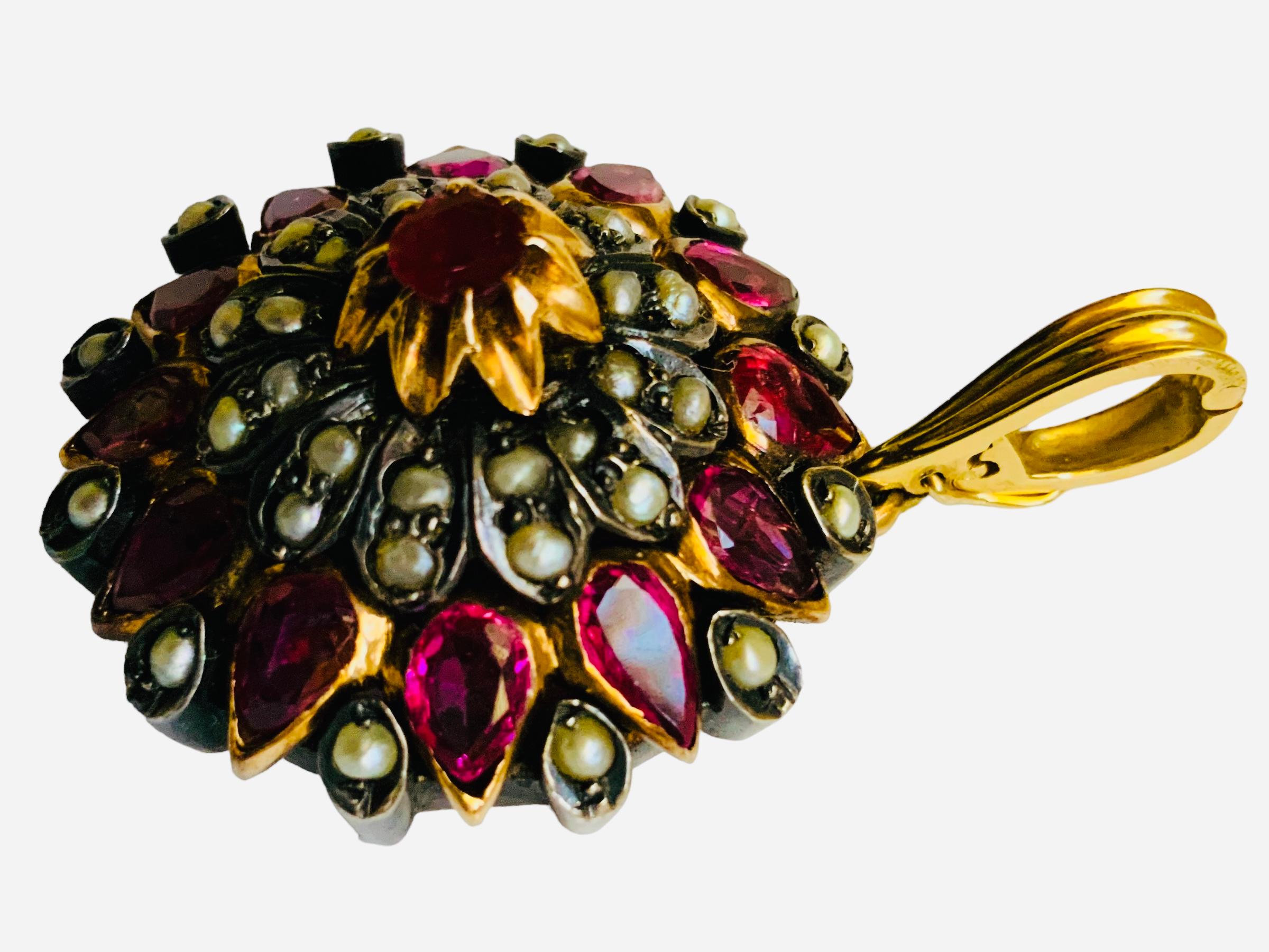 This is a Victorian style Rose Gold Rubies and Seed Pearls pendant. It is a round pendant shaped as a flower and decorated with petals made of marquise cut rubies in rose gold bezel setting alternated with 12 embedded seed pearls. Above them, there