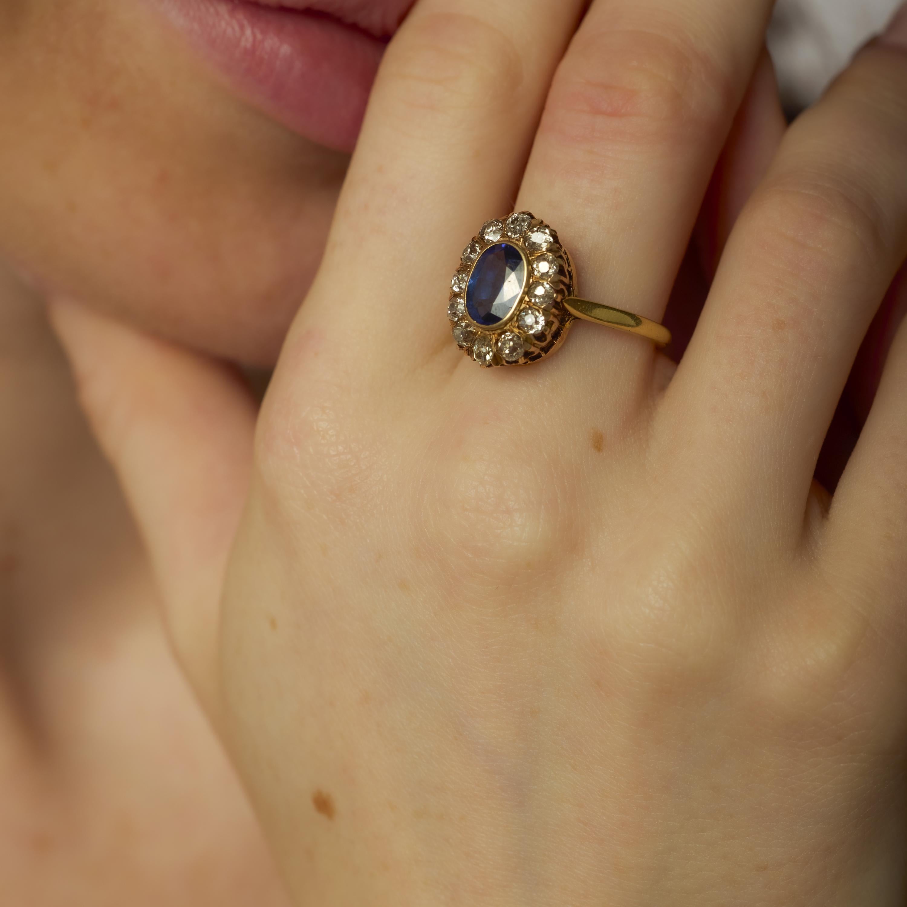 Questo anello di ispirazione vittoriana è incentrato su uno zaffiro blu taglio ovale da 1,40 carati, che emana eleganza e profondità. Intorno alla vibrante pietra centrale ci sono dodici diamanti taglio old mine, le cui sfaccettature antiche