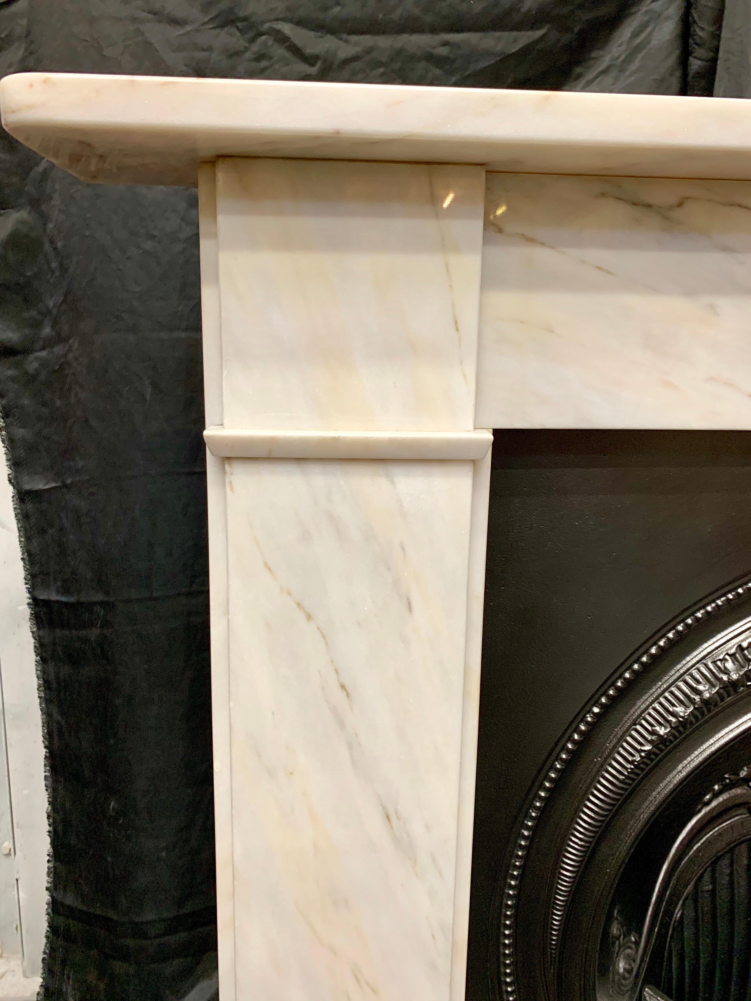 A handsome period Victorian style lightly veined statuary marble fireplace surround of simple form. A square shelf sits above a plain frieze, flanked by stepped jambs with splayed separation moulding to lower frieze line, all resting on moulded foot