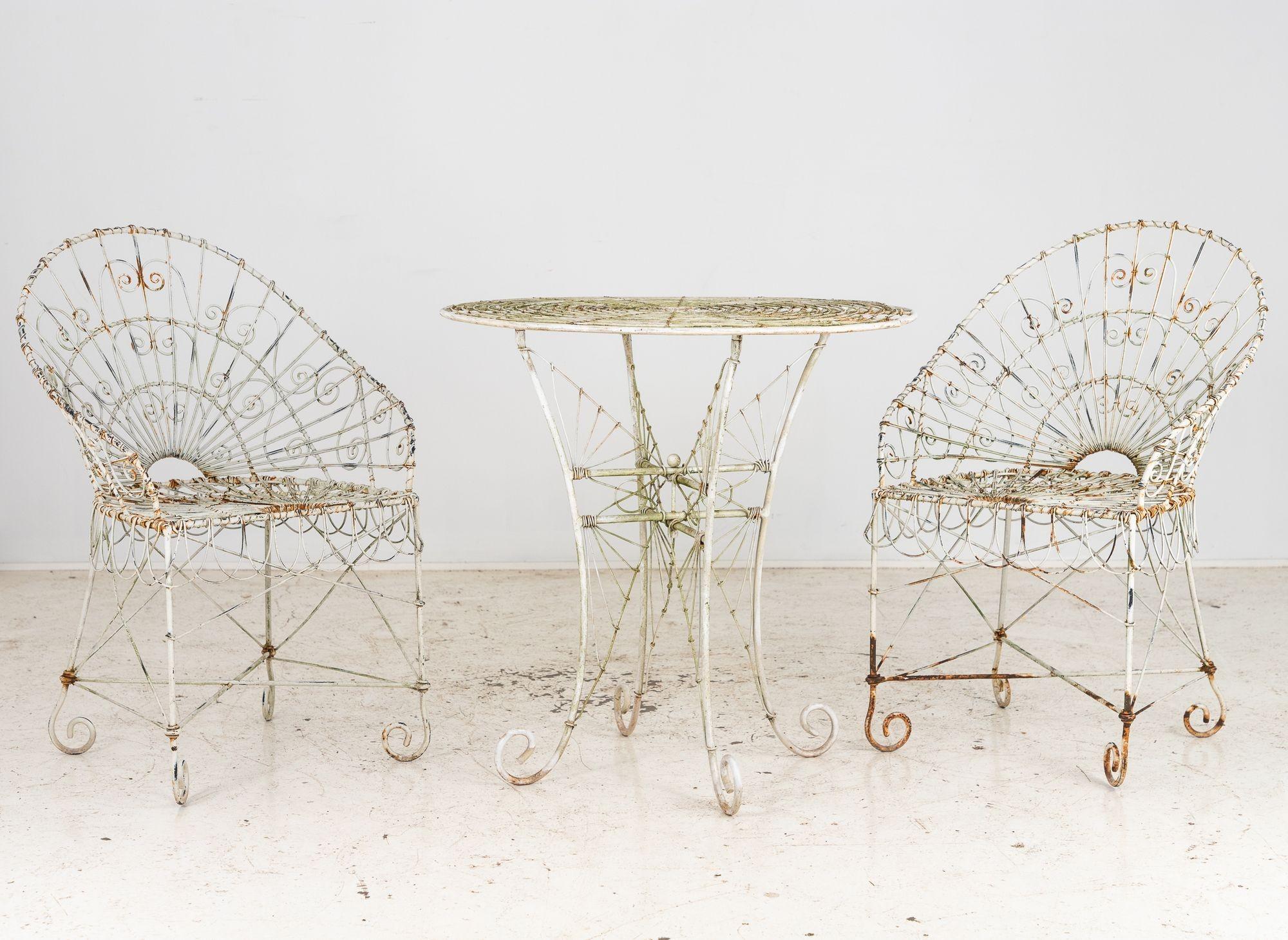 Questa coppia di tavolo e sedie da caffè in filo metallico in stile vittoriano, proveniente dalla Francia degli anni '60, presenta intricate volute ripetute sugli schienali, sulle gambe e sulla base del tavolo. La vernice bianca è incantevolmente