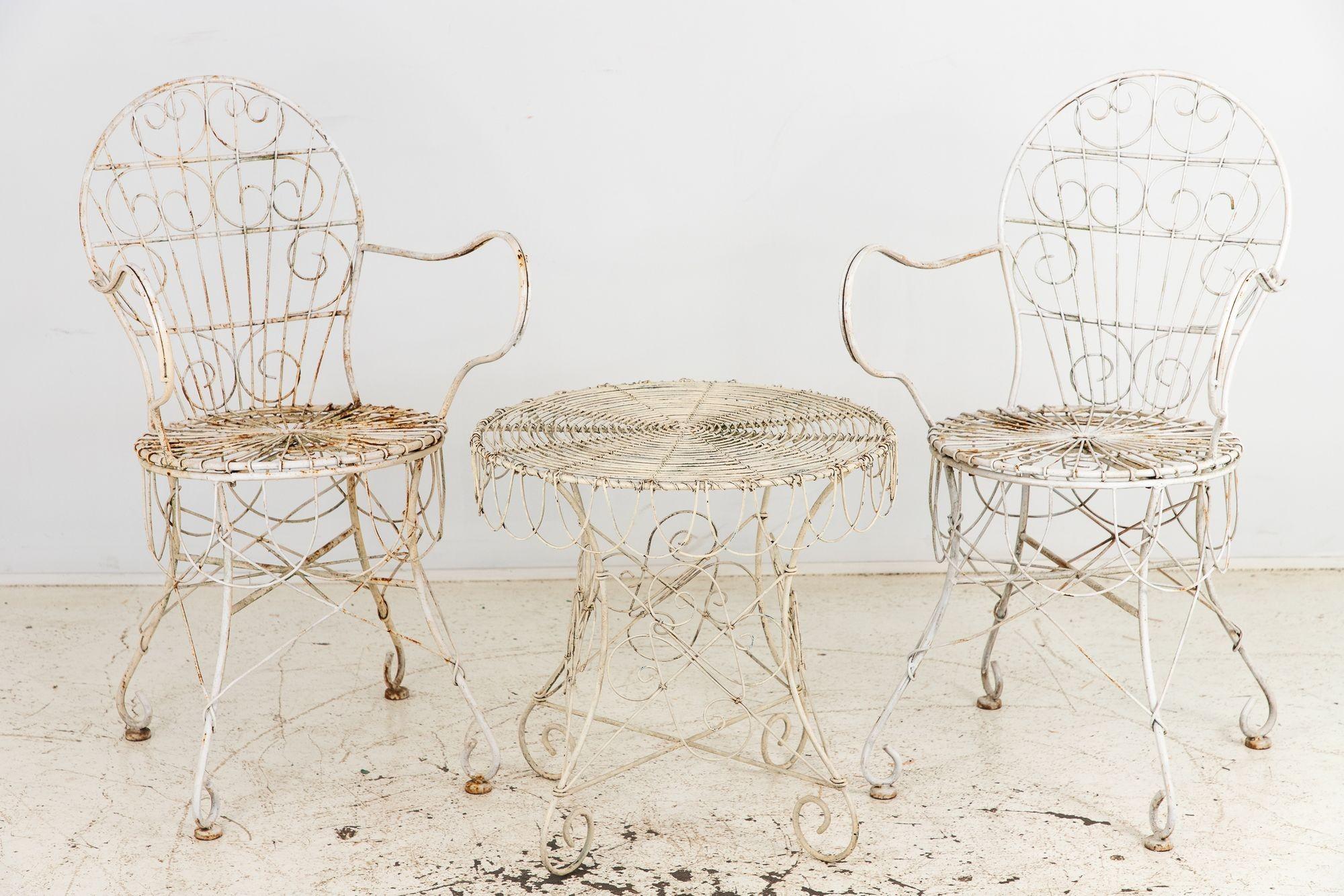 Cette paire de tables et de chaises de café en fil de fer de style victorien, datant des années 1960 en France, présente des volutes répétitives complexes sur les dossiers, les pieds et la base de la table. La peinture blanche est délicieusement