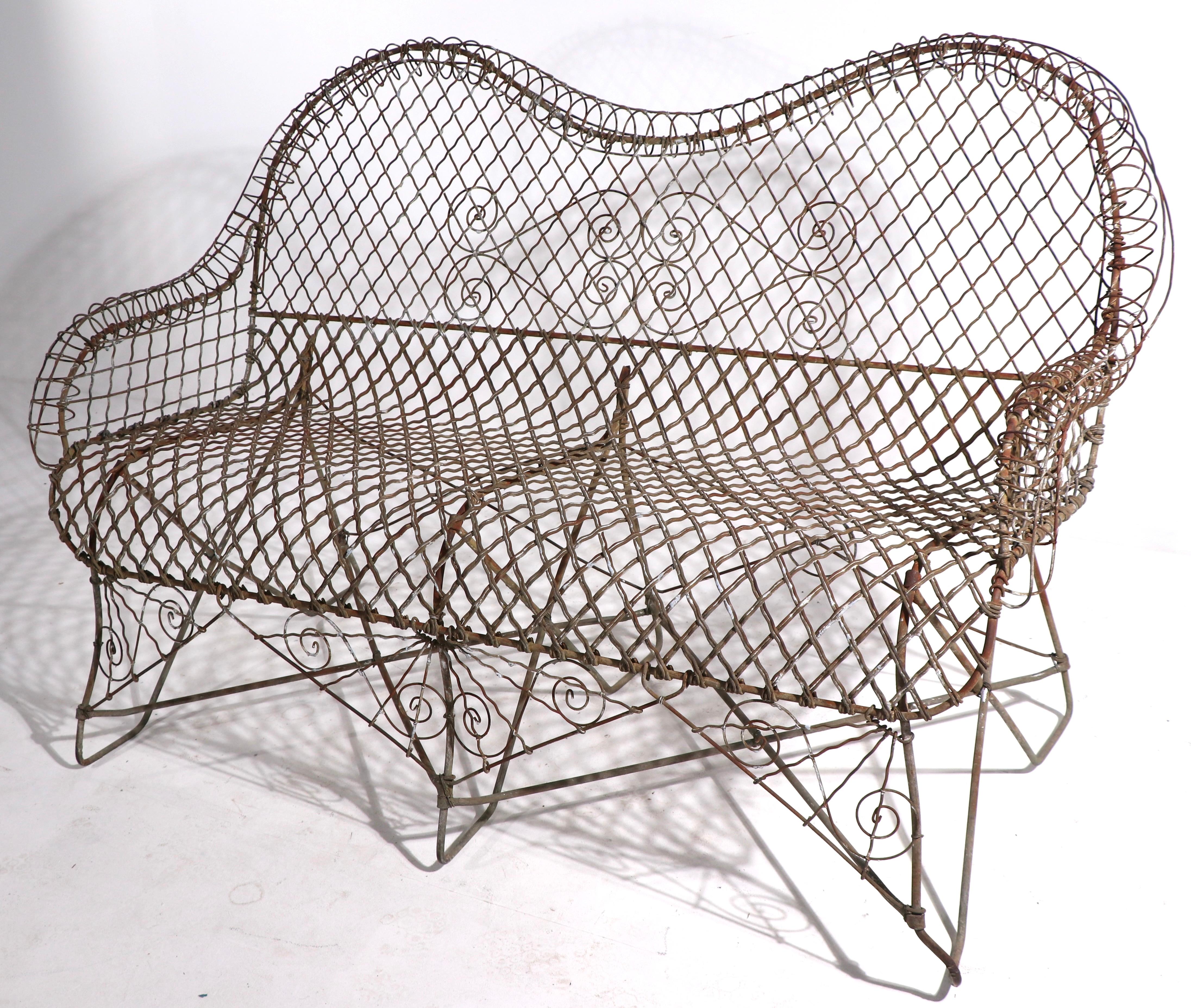 Charming Victorian style garden settee having a wire and woven metal seat and back, with wrought iron legs . This example is early 20th C vintage, it is in very good, original condition, showing expected cosmetic wear to finish, normal and