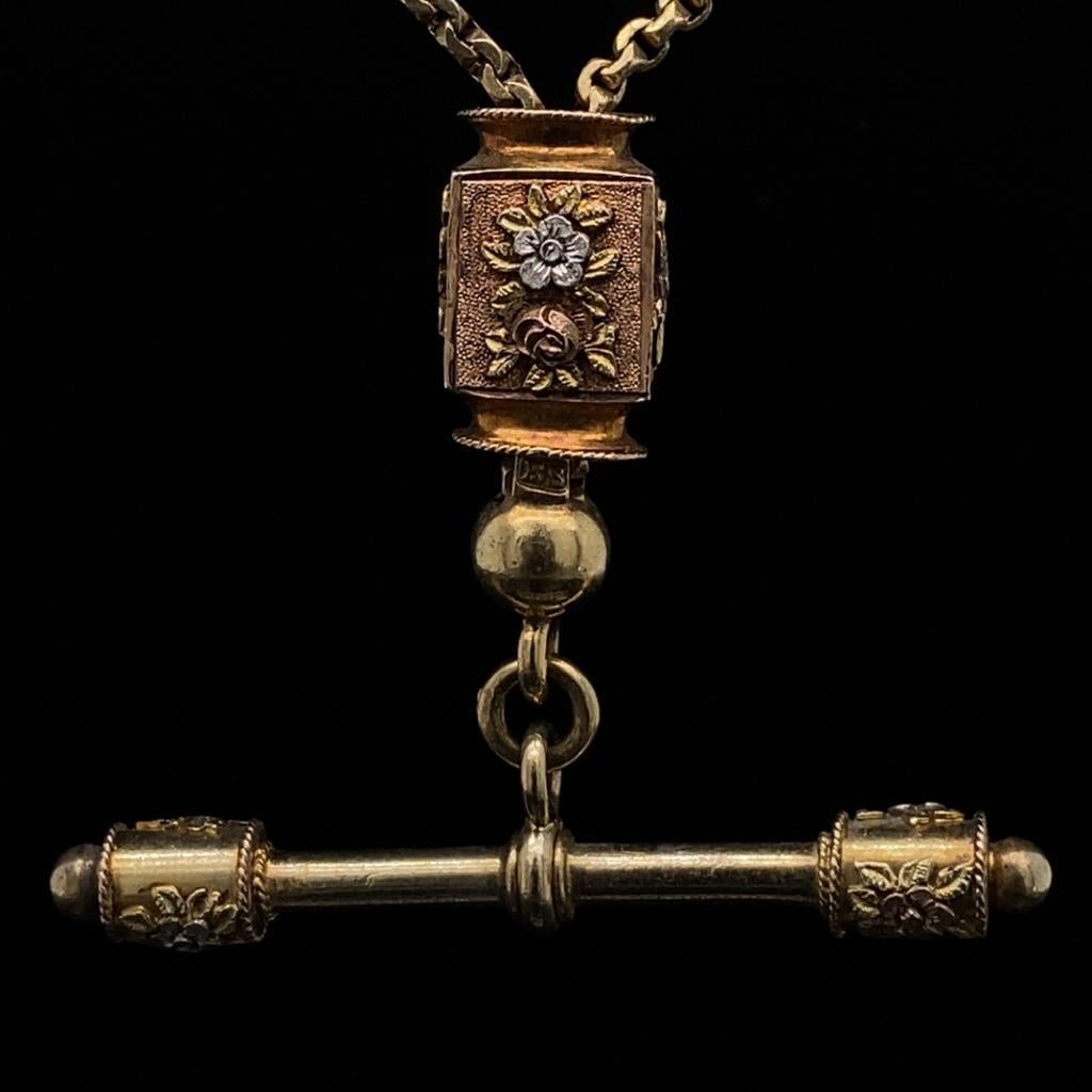 A T Bar Chain in 15 karat yellow gold, circa 1880.

This excellent example of Victorian craftsmanship boasts a movable rose gold rectangular section engraved with ornate floral detail, this is mirrored in the fine gold wire flowers found either side