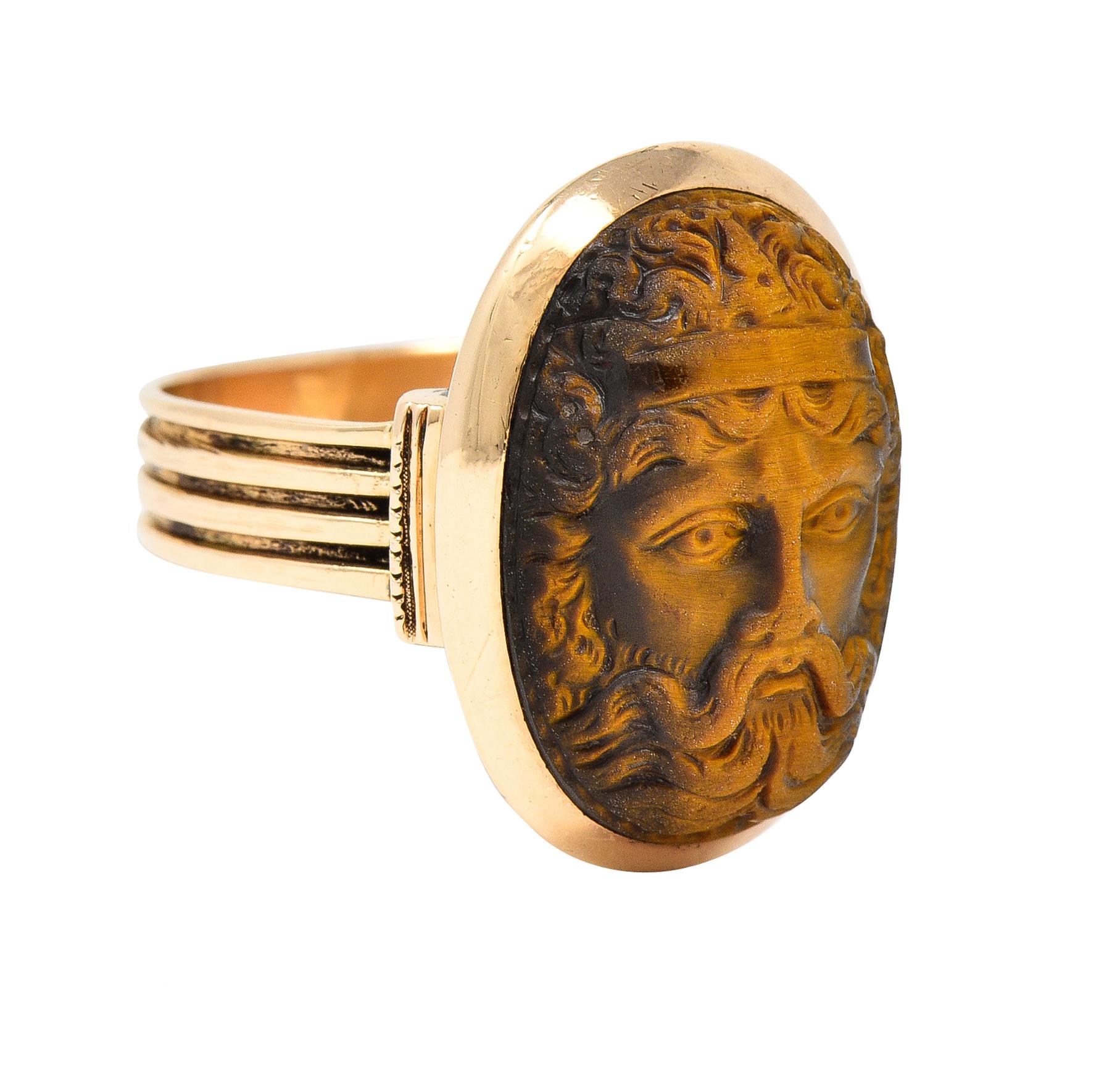 Centering a tigers eye measuring 13.0 x 18.0 mm - carved to depict the Greek hero, Hercules
With curling hair and headband - opaque with dark to light brown banding and slight chatoyancy
Set in an oval-shaped bezel and flanked by column-like