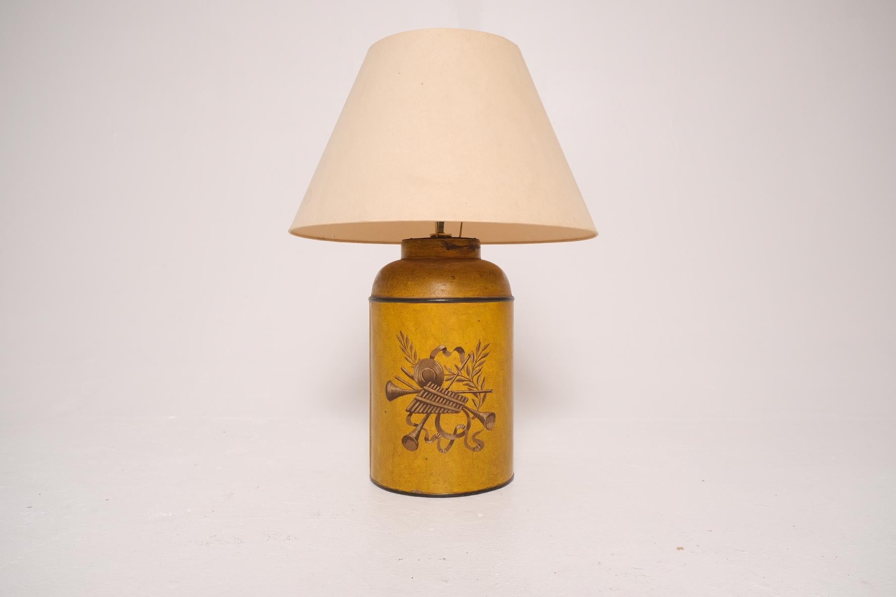 A late 19th-century English toleware tea canister, converted into a table lamp, attributed to Parnall & Sons of Bristol. This cylindrical tin canister is finished in a rich ochre yellow with hand-painted classical motifs—featuring a bundle of