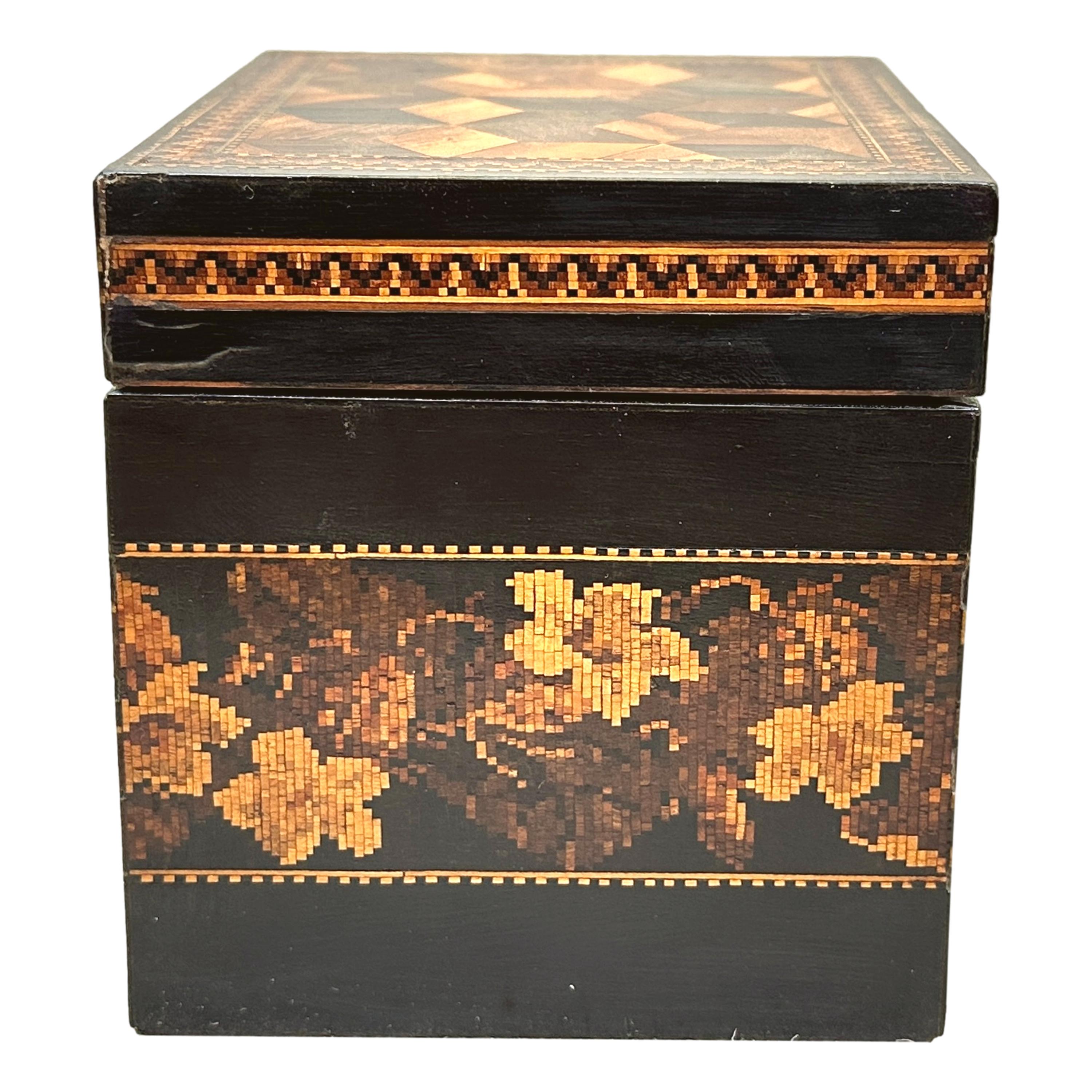 A Charming 19th Century Tunbridge Ware Tea Caddy With Attractive Floral Band To Main Body And Parquetry Perspective Cubes To Hinged Lid Enclosing Lidded Interior.


Tea was an extremely valuable commodity throughout the course of the 18th and 19th
