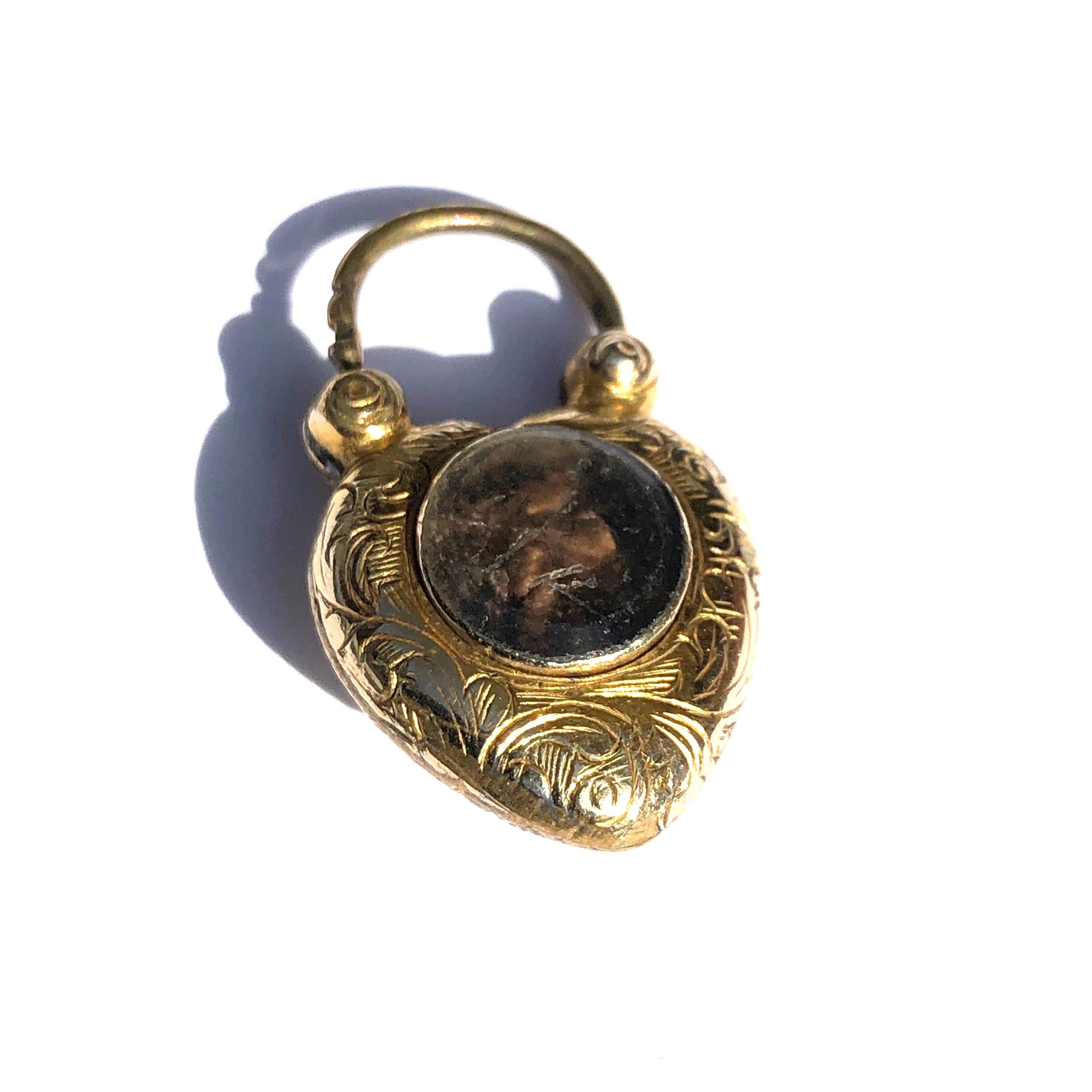 The heart shaped padlock features exquisite scroll leaf engraving and a cluster in the shape of a flower with turquoise petals and a ruby centre. On the other side of this pendant is a glazed locket holding a lock of hair. 

Height: 1inch 

Weight: