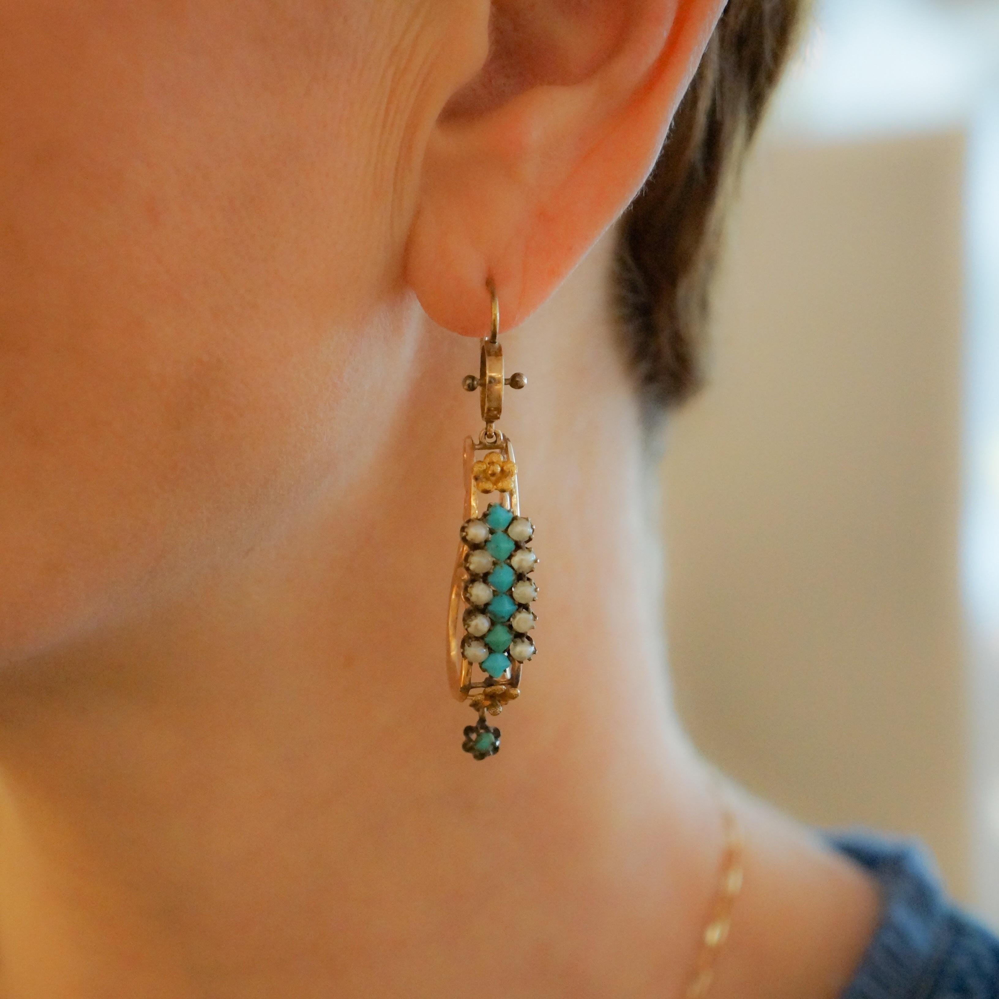 A pair of Victorian 14 karat gold and silver earrings with turquoise and pearls. The earrings have a center row of 7 turquoise cabochons framed with 10 freshwater pearls each and an articulated gold bead hanging from a decorative back.   Circa