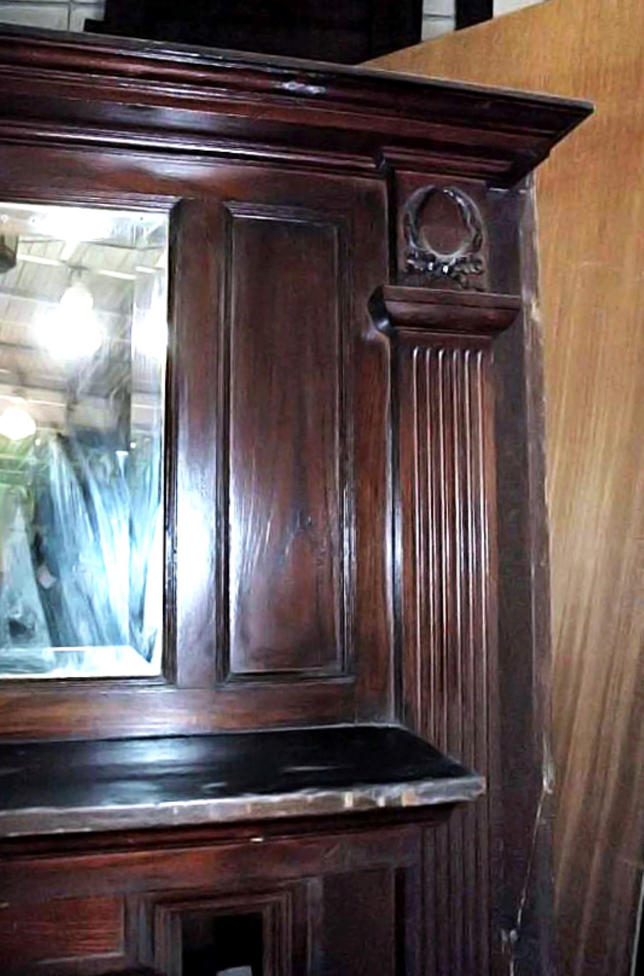 Victorian wood mantel with a hand carved wreath motif in center, circa late 1800s. It has the dark mahogany original finish and features the original beveled over mantel mirror. Wear is consistent with age. This can be seen at our 400 Gilligan St