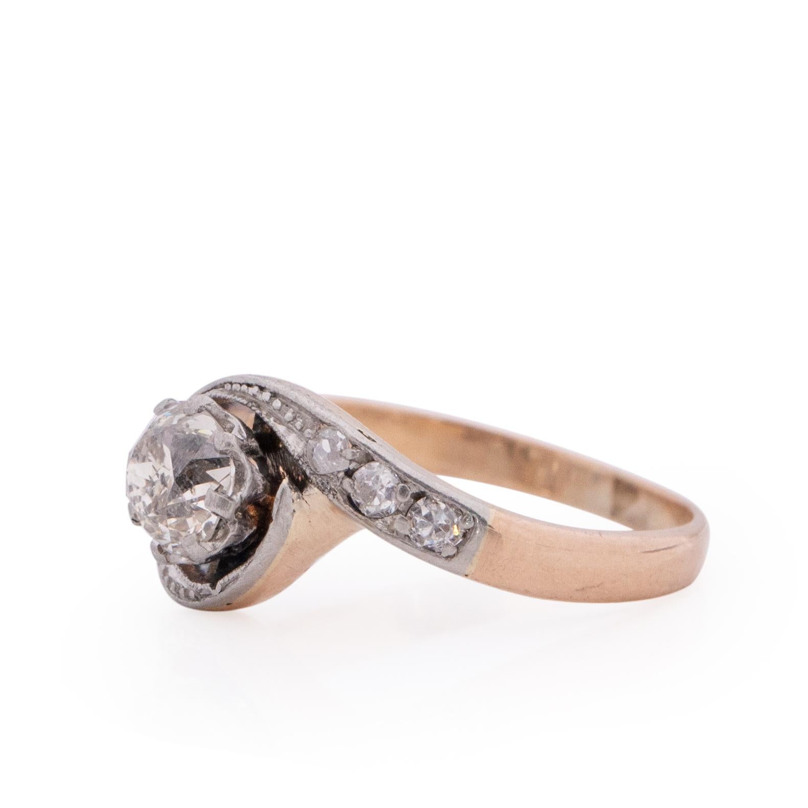 This is a classic example of a Victorian ring. Sitting the the two tone platinum and rose gold setting is a beautiful chunky old mine cut diamond. encompassing the center diamond is the winding shanks of the ring, in the platinum is six beautiful