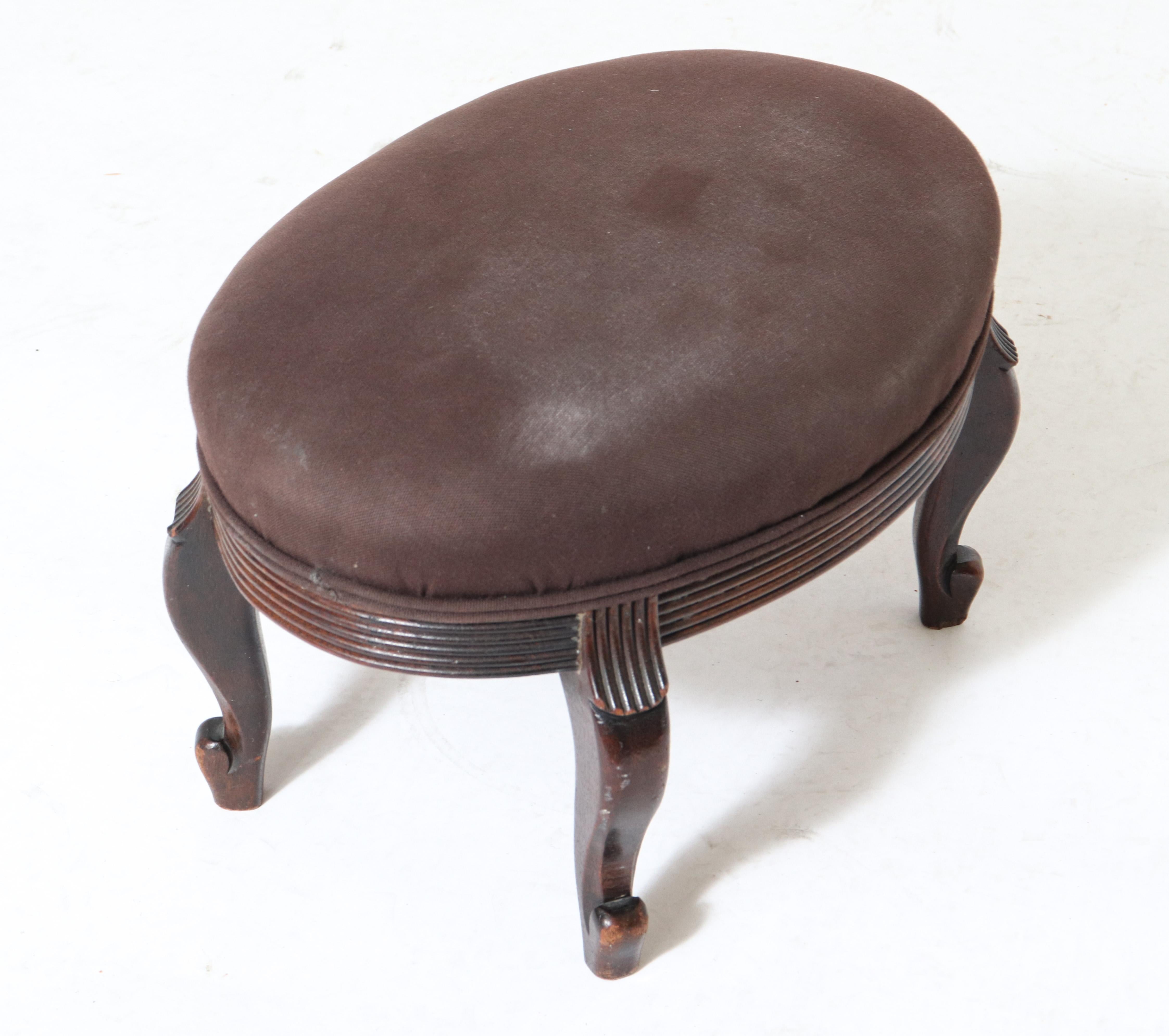Victorian upholstered petite oval footstool with brown tone upholstered cushion and wood frame with carved ribbed detailing.