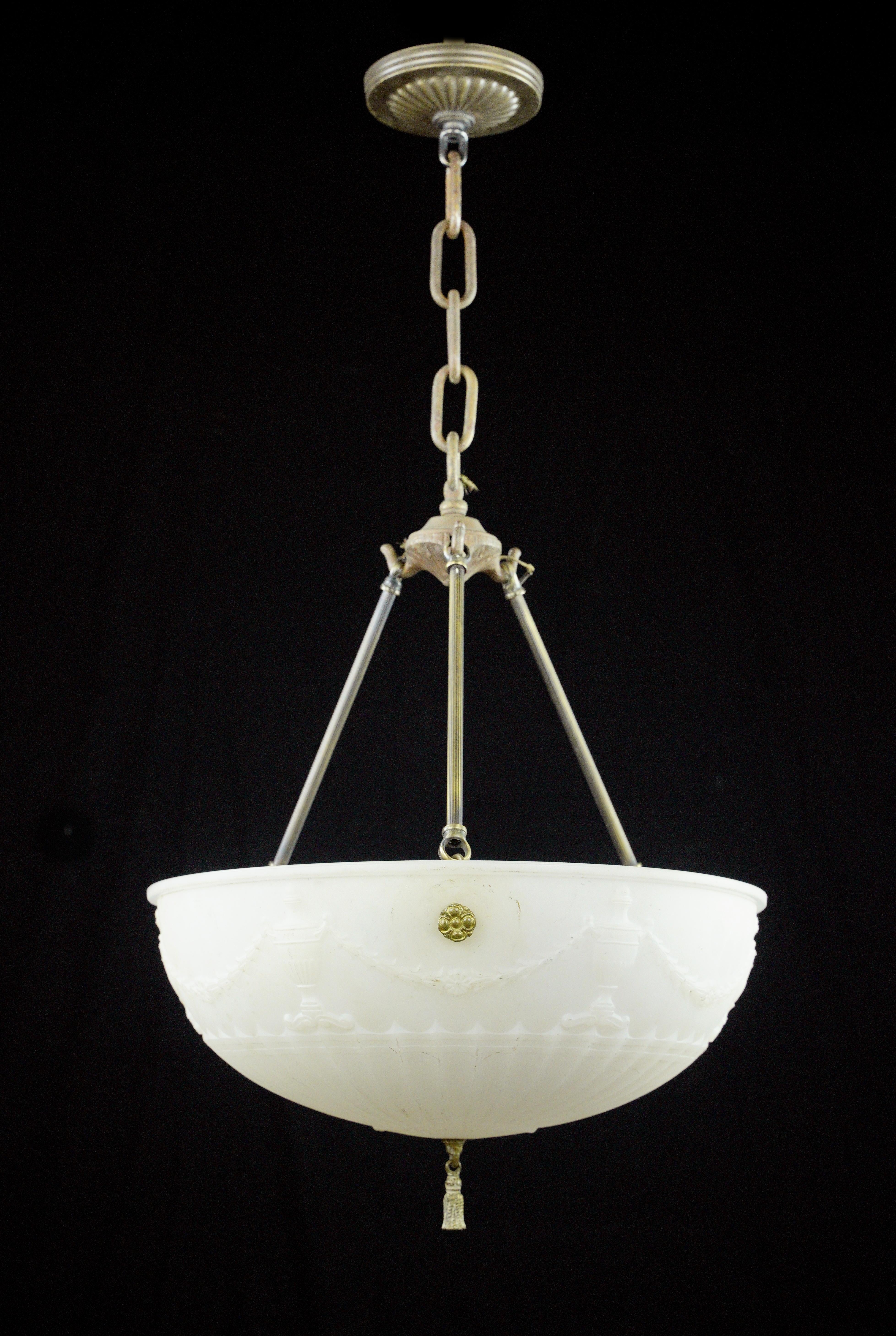 This Victorian brass pendant light embodies vintage charm. Its white cast glass dish with a radial urn design exudes elegance, complemented by a brass fixture, making it a captivating addition to any Victorian inspired decor. Takes three standard