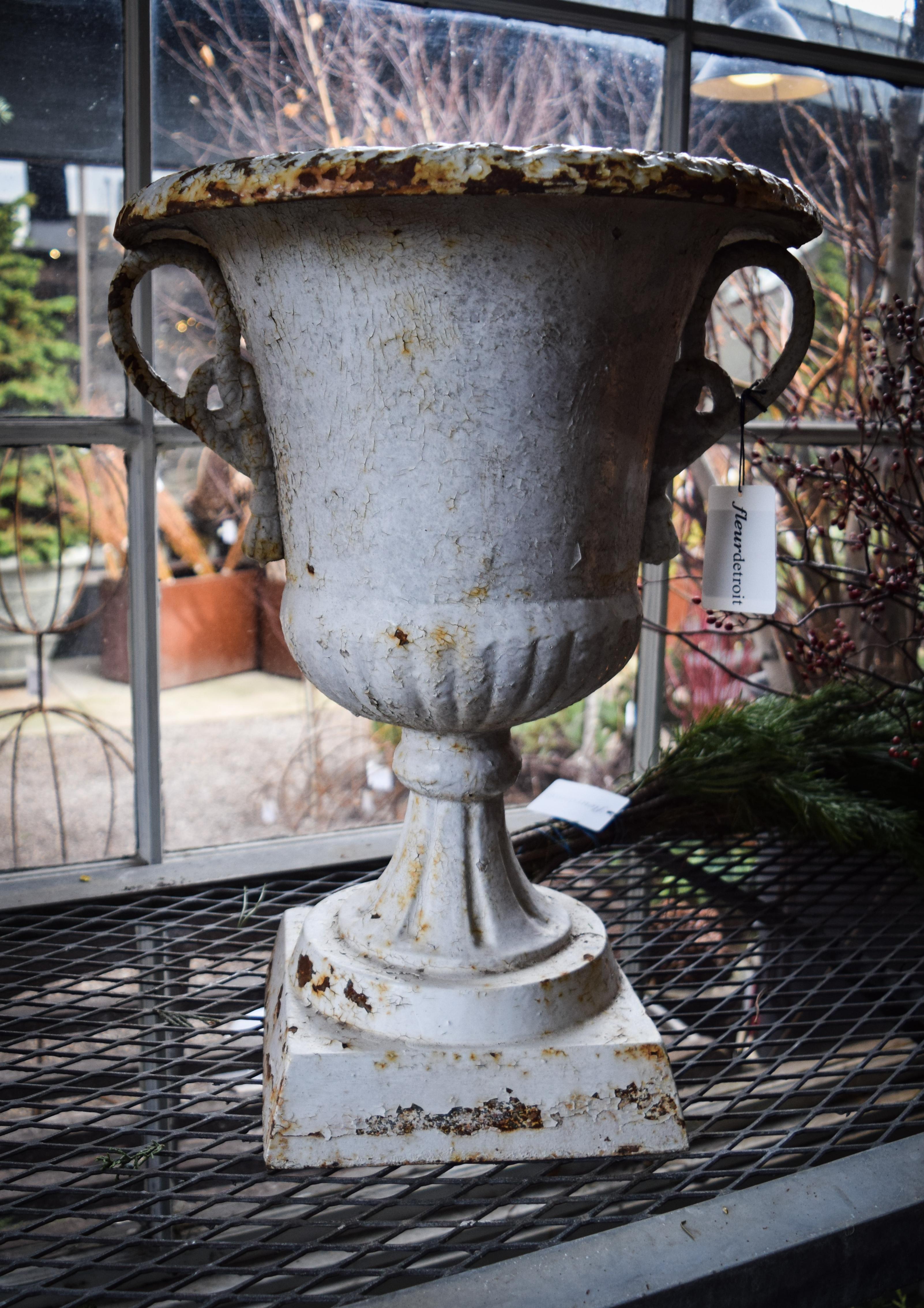 This pair of beautifully weathered iron Victorian urns are a beautiful accent for any season. Perfectly rusted, the crackled paint adds a dignified, vintage flair. Handles feature a charming rope and tassel detail. This set of one of a kind