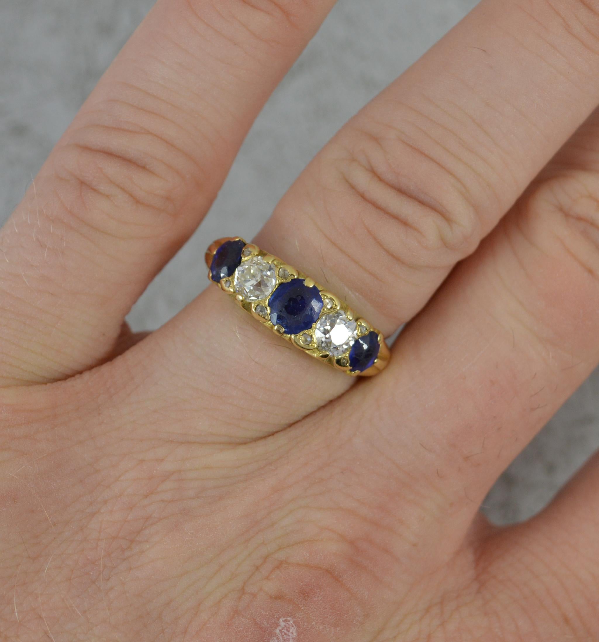 A fine 18 carat gold, sapphire diamond five stone ring. c1880.
18 carat yellow gold shank and setting with deep floral scroll work.
Designed with alternating natural blue sapphires and old European cut diamonds with additional small diamond chip