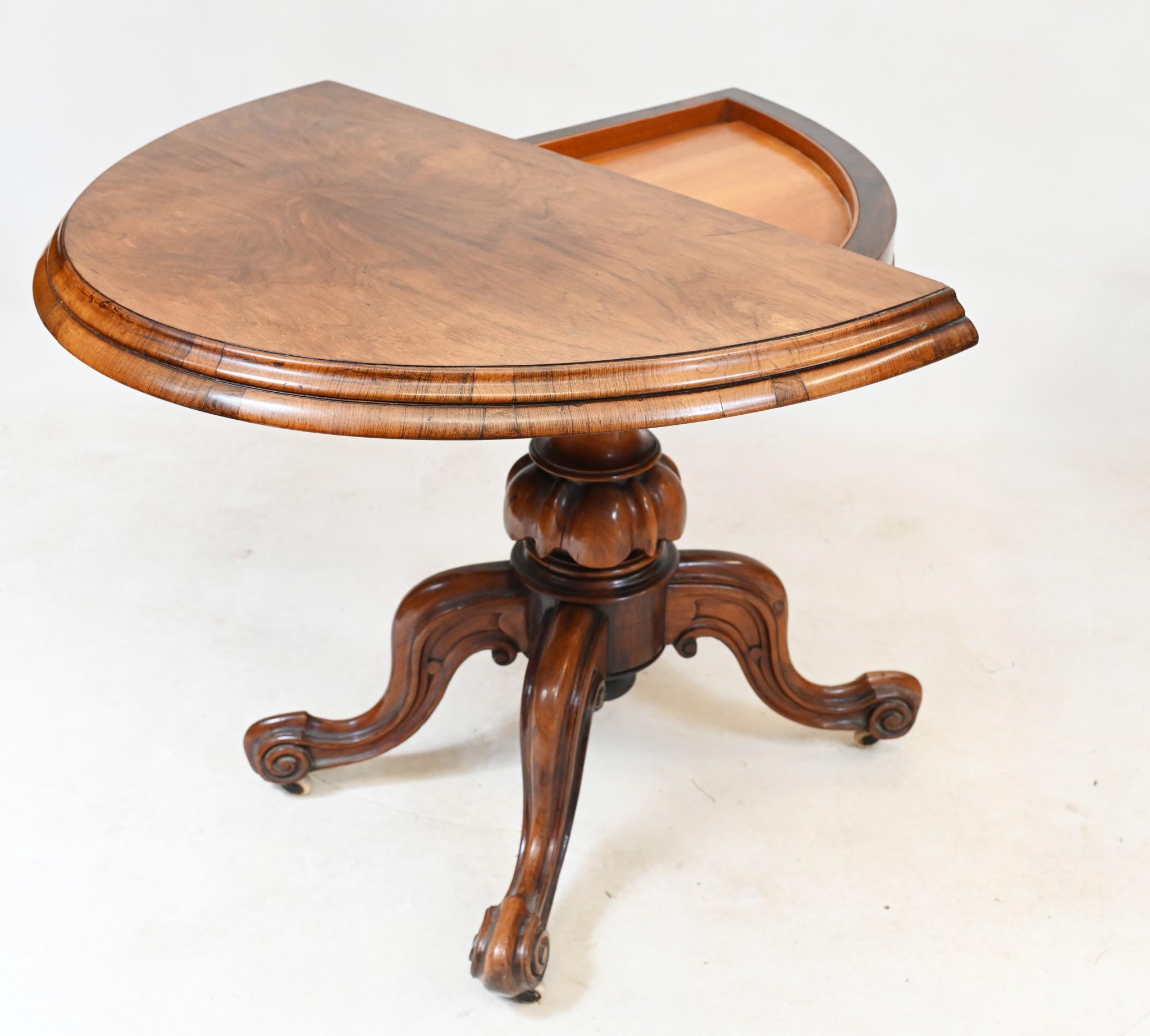 You are viewing a gorgeous period Mid Victorian card or games table in walnut
Features an elegant base with tulip design to main support
Top is of demi lune - half round - form
Top opens up to reveal red beized lined playing surface
For today's
