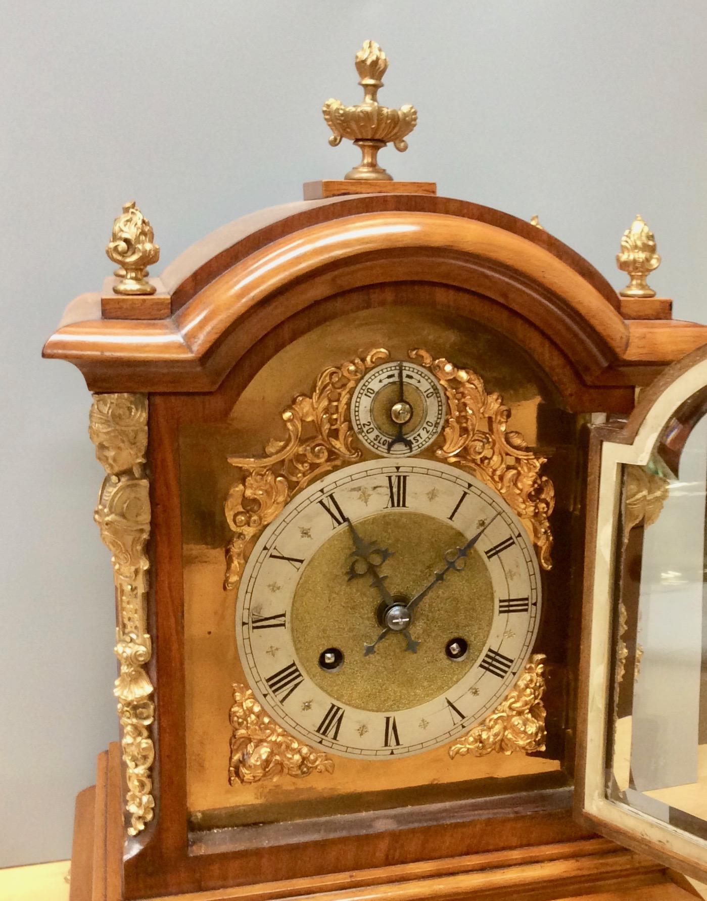Late Victorian walnut break arch mantel clock standing on a raised plinth and resting on four outswept gilded paw feet and surmounted by four flame finials and a central finial.

Heavy beveled glass door opening to a brass dial with finely matted