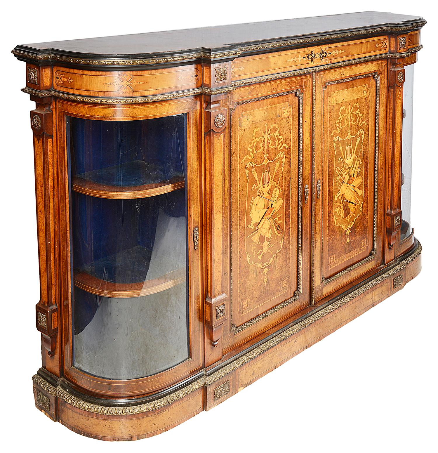 A very good quality Victorian period Walnut credenza, having bow glass to either side with shelves within. The two central doors each with wonderful marquetry inlay, depicting musical instruments and raised on a plinth base.