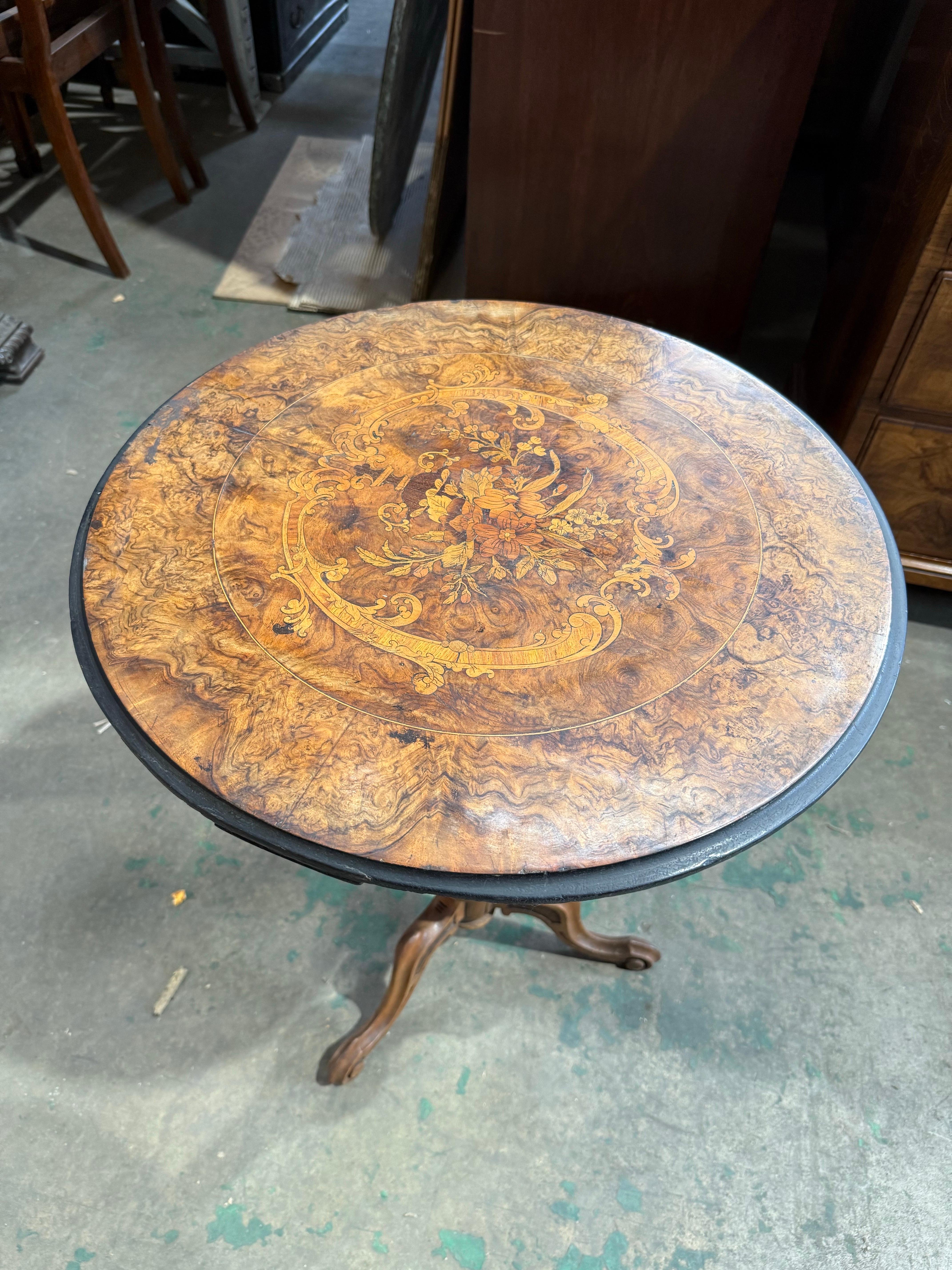 Preciosa mesa auxiliar de nogal de la época victoriana, con tablero circular ricamente labrado y adornado con una intrincada marquetería floral. La incrustación central muestra un ramo de flores en una urna clásica, bordeada de motivos de acanto,