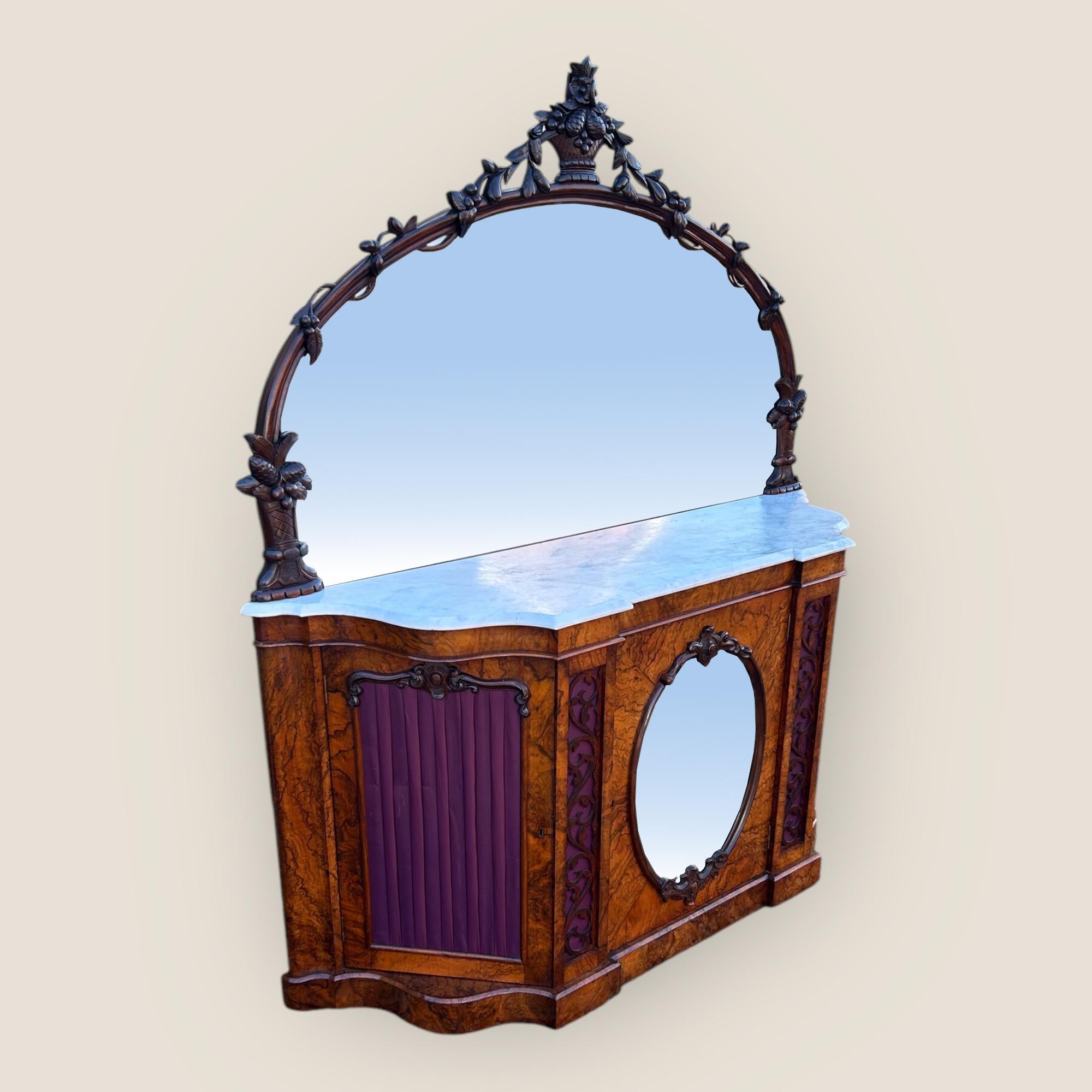A Victorian Walnut Mirror Backed Sideboard of serpentine shape with beautiful walnut veneers and a bevelled white marble top. To the back is a magnificent carved mirror with floral carvings showing vines intertwined from the bottom to the top carved
