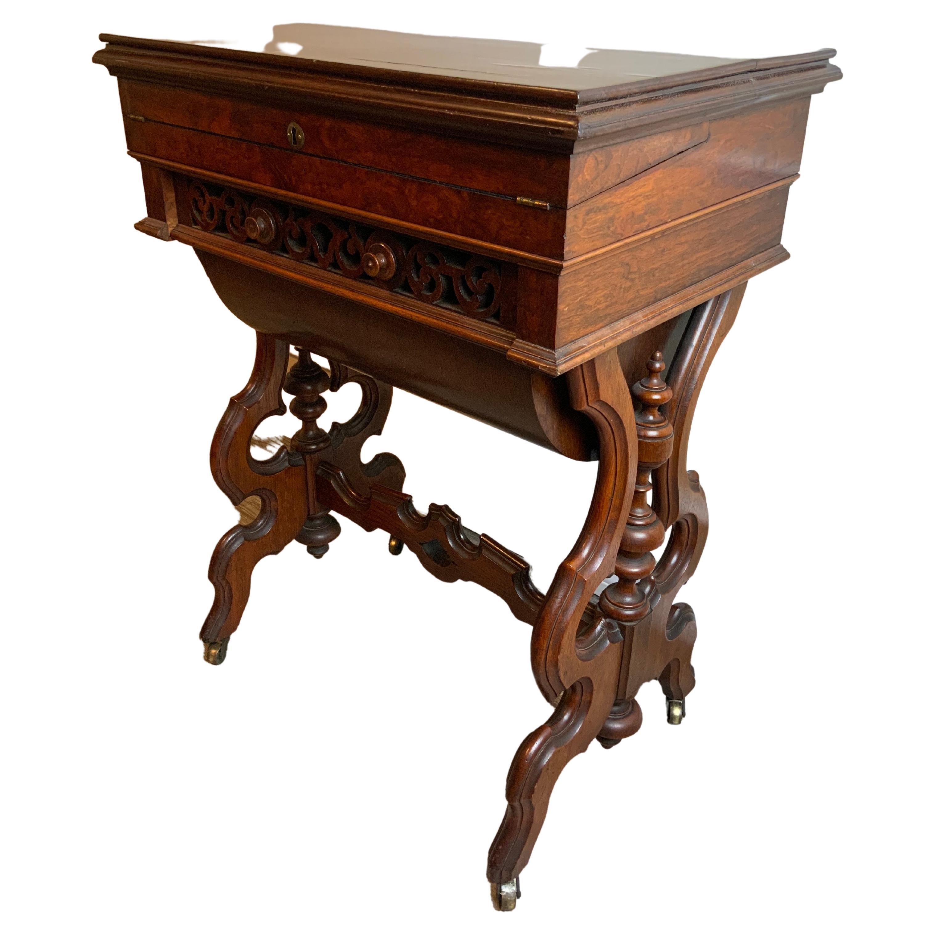 A very nice earl Victorian Burl walnut sewing stand and work table in very good condition.  This unique piece has a fold out writing or work surface under the top lid as seen often in writing slopes or lap desks. There is a large pierced carved pull