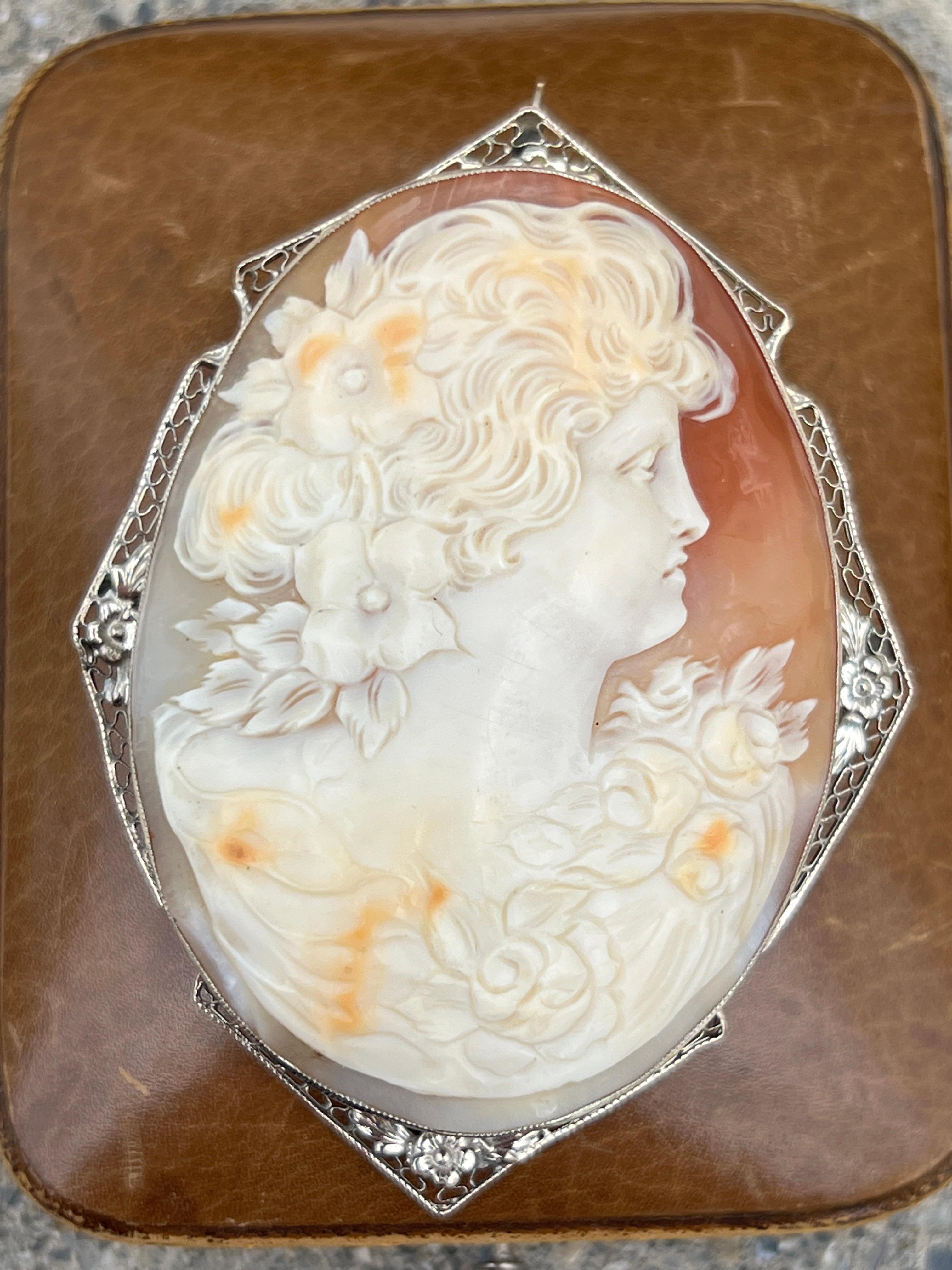 Discover the timeless elegance of this 1920s art deco 14 karat white gold brooch, featuring a beautifully carved shell cameo set within a delicate floral filigree frame. This versatile piece, measuring 2.9 by 2.1 inches and weighing 21.88 grams, can