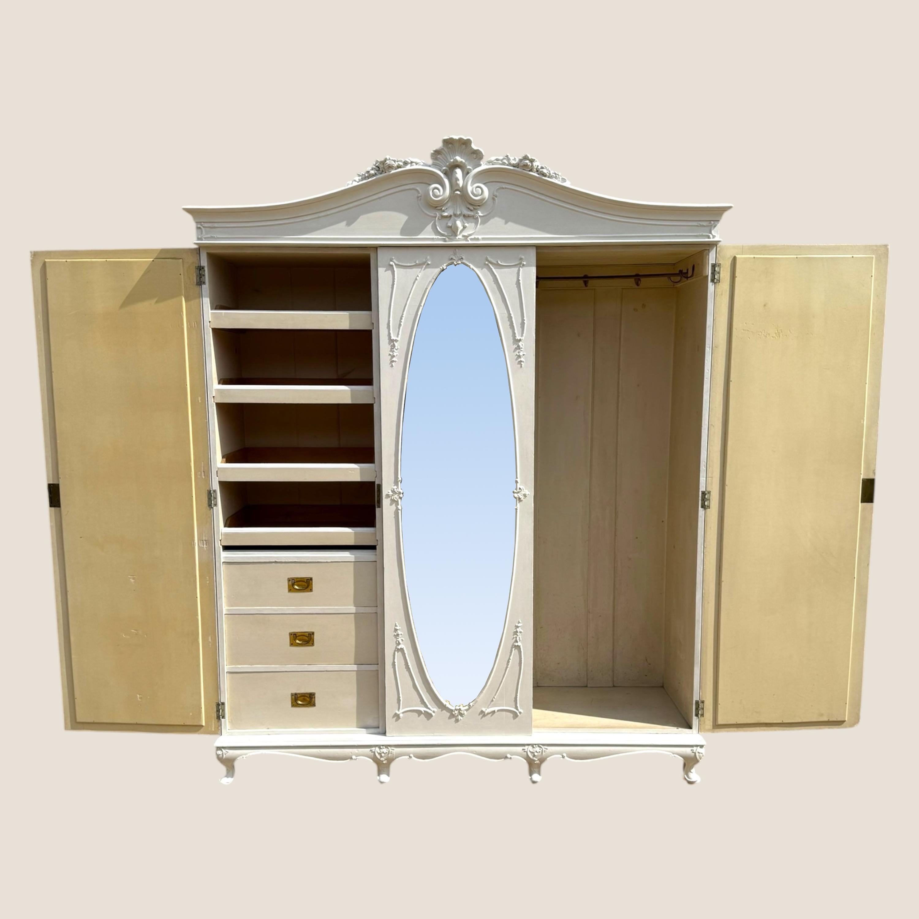 Here we have a rustic style Victorian, circa 1890, white painted 3 door wardrobe with all original handles and parts. Detailed with rococo mouldings and carvings on each door and the central door has a large oval bevelled mirror also surrounded with