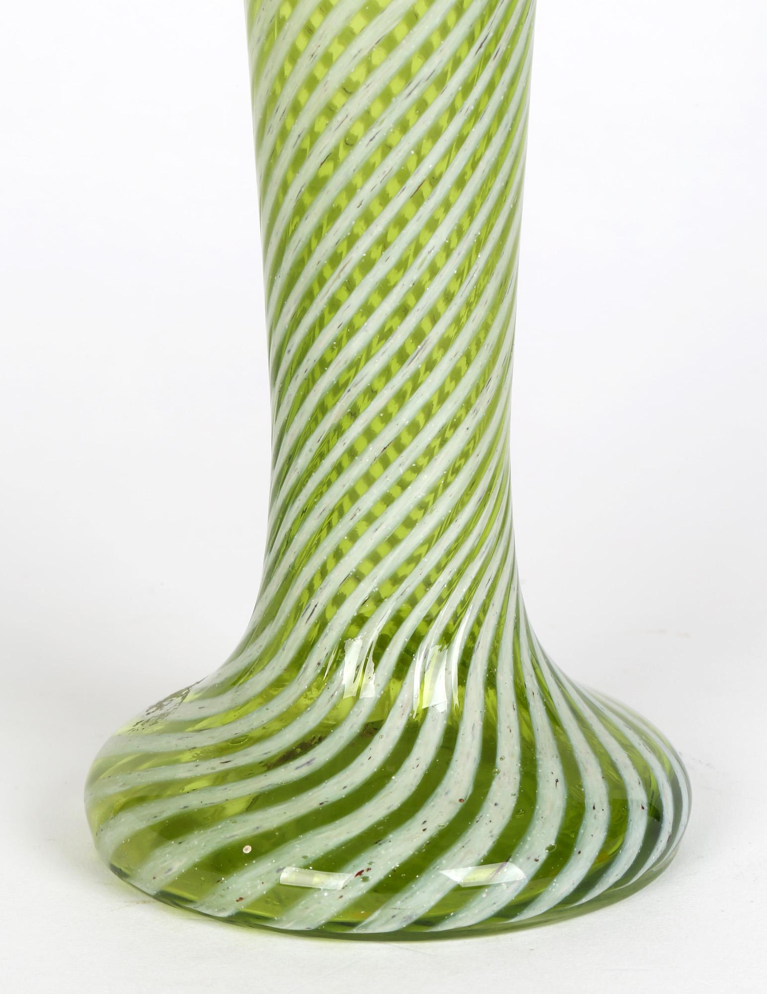 Un elegante vaso antico in vetro verde a strascico bianco, probabilmente inglese e risalente al 1890 circa. Il vaso alto e sottile ha una base cava e arrotondata, con un collo alto a forma di tromba e un'ampia sommità a forma di fiore. Il vaso ha