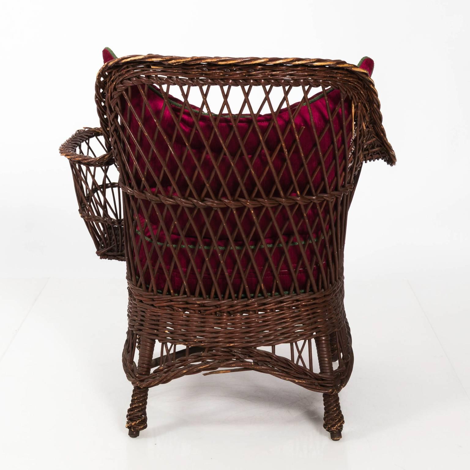 Pair of natural woven wicker American Victorian chairs by Heywood Wakefield and Co. with braided trim and custom red upholstered cushions. One features a magazine pocket, circa 1880.