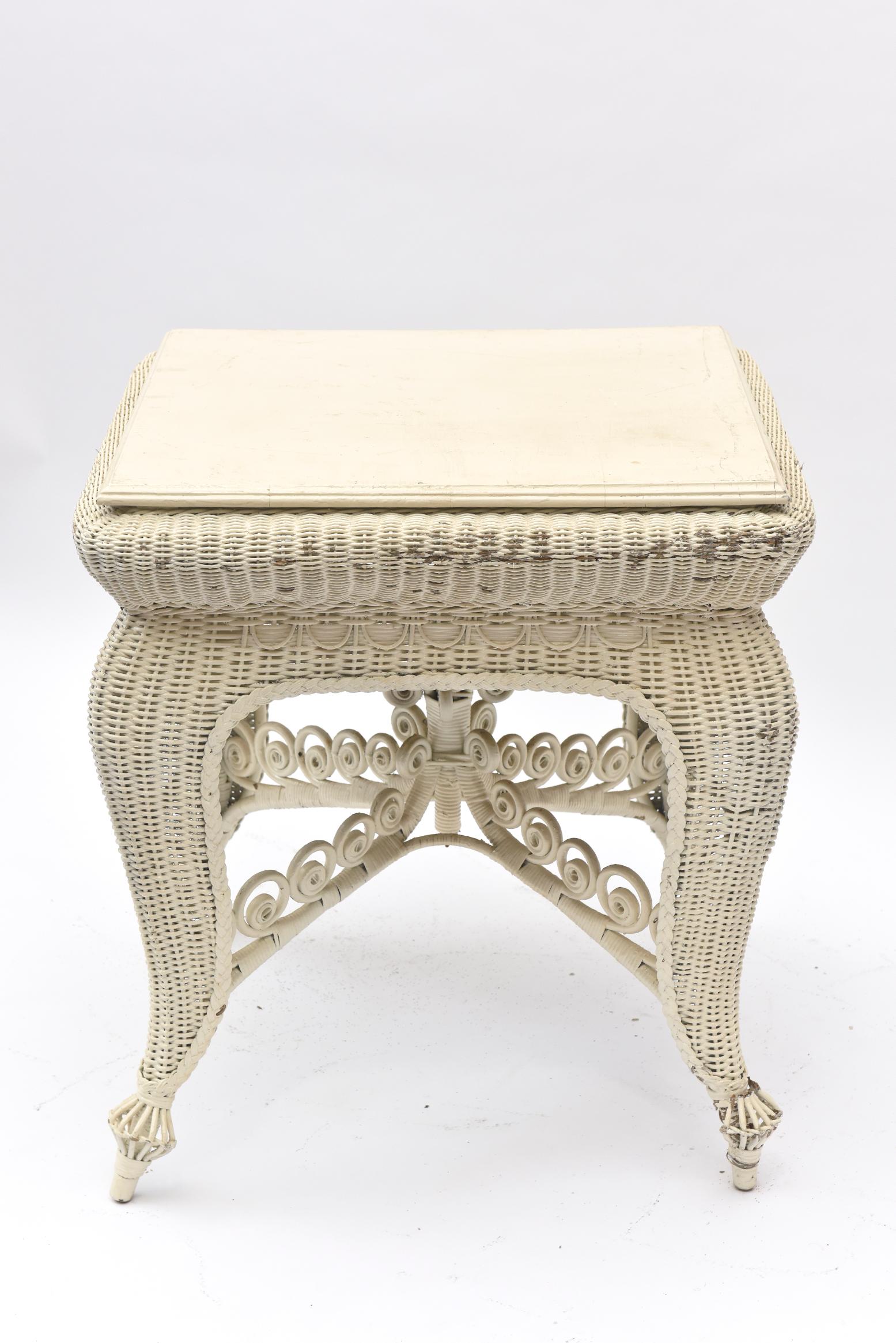 This lovely square table is tightly woven and has beautifully curved legs and a crisscrossed curlicue base. At the base of the legs is a 