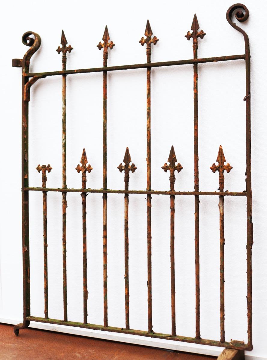 A reclaimed wrought iron side gate with repeated pointed finials and decorative scrolls to the top.