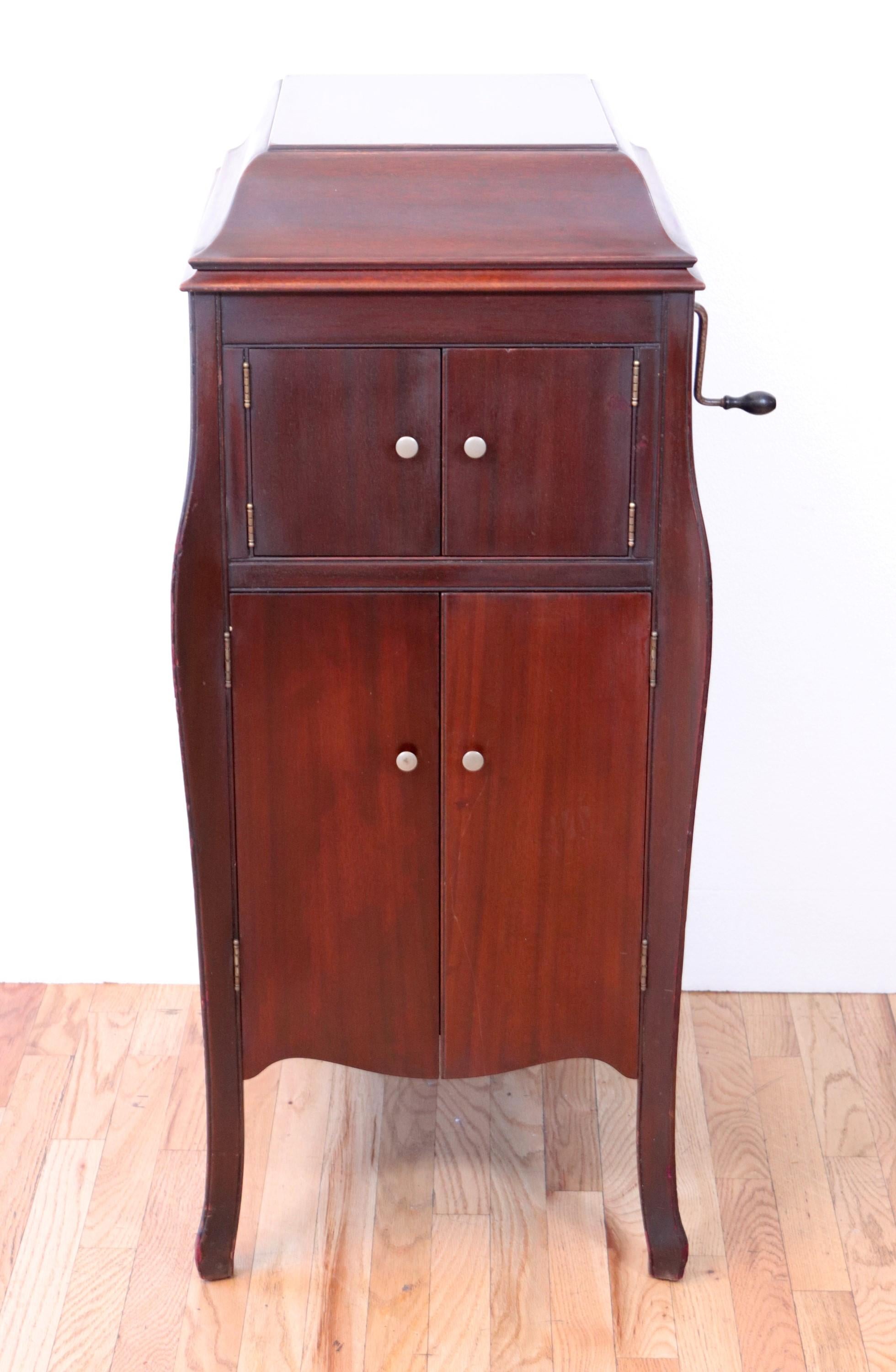 VV-X Victrola Phonograph, wind up record player with ten 78 rpm records. This Model number VV-X 147174J, was manufactured by The Victrola Talking Machine Company. Underneath the phonograph is a mahogany wood cabinet for storage. There is also a wood