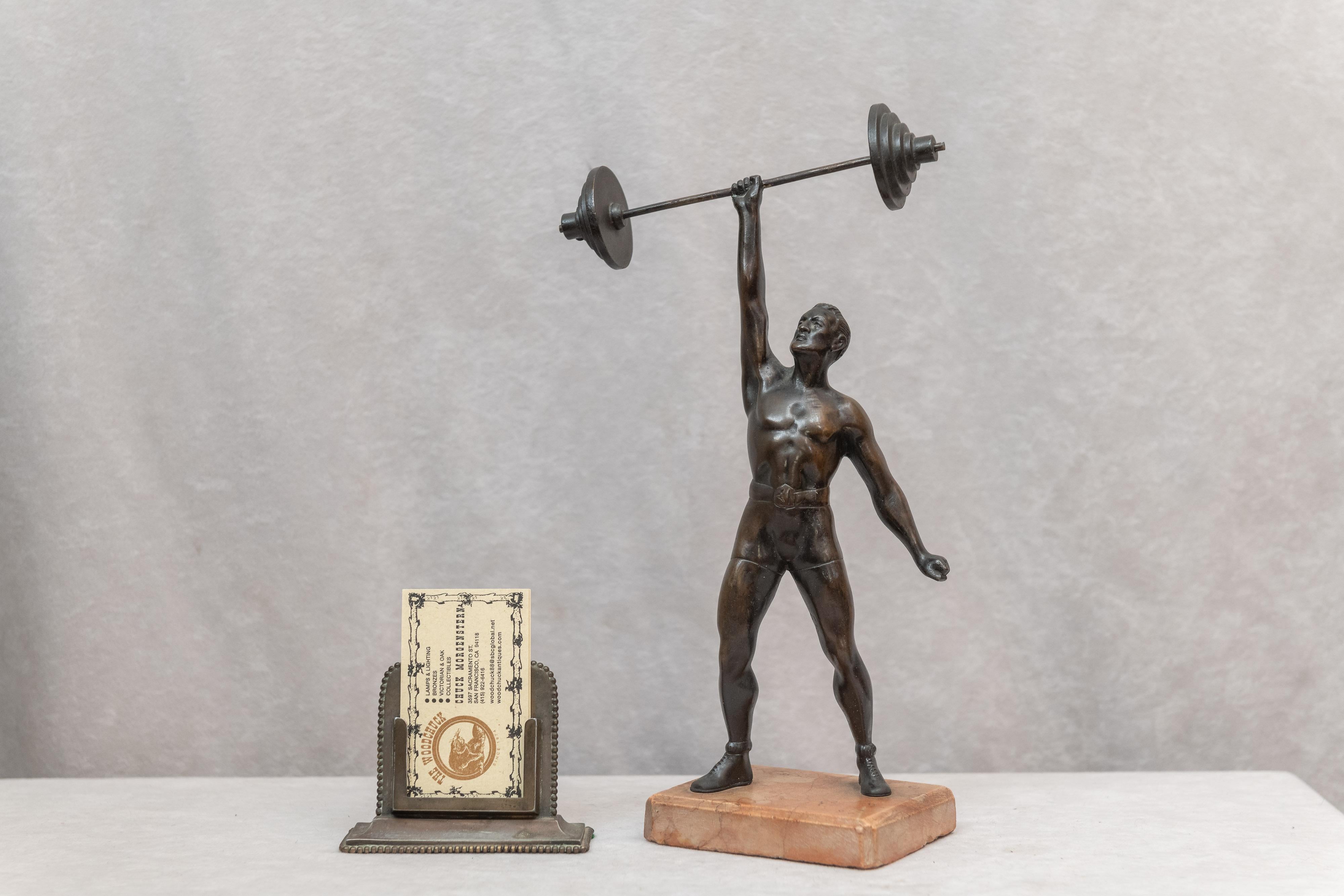 Offering here a most unusual bronze figure of a weightlifter applying his strength and skill as he lifts a barbell with a single arm over his head. That is very strong. How do we know this was made in Austria and is considered a Vienna bronze? I