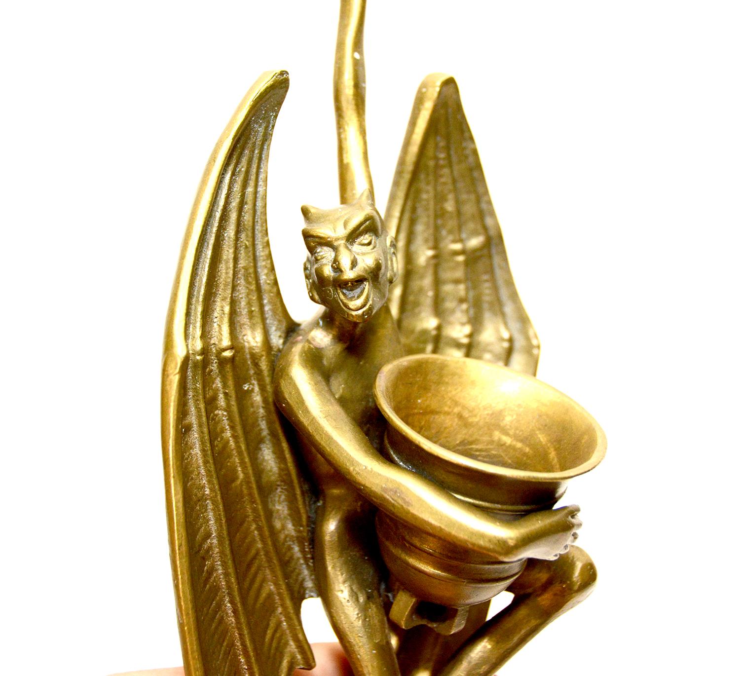 This is a rare whimsical Devil figure wall hanging match holder. The winged devil is holding a large vase in front of his chest. The vase can be used to store matches. His long stretched arm and hand hold a ring, which allow you to easily hang this
