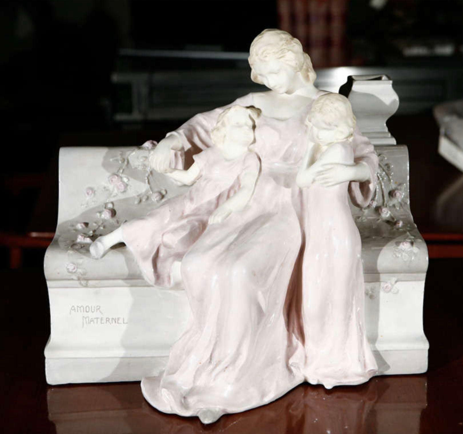 Eine Wiener Fayence-Porzellanfigur mit der Darstellung der Mutterliebe von Schauer. Bank und Figuren sind aus Porzellan. Die Gesichter und Arme sind aus Biskuit (flach). Auf dem Boden gestempelt: Vienna Faience Schauer. Außerdem ist auf der