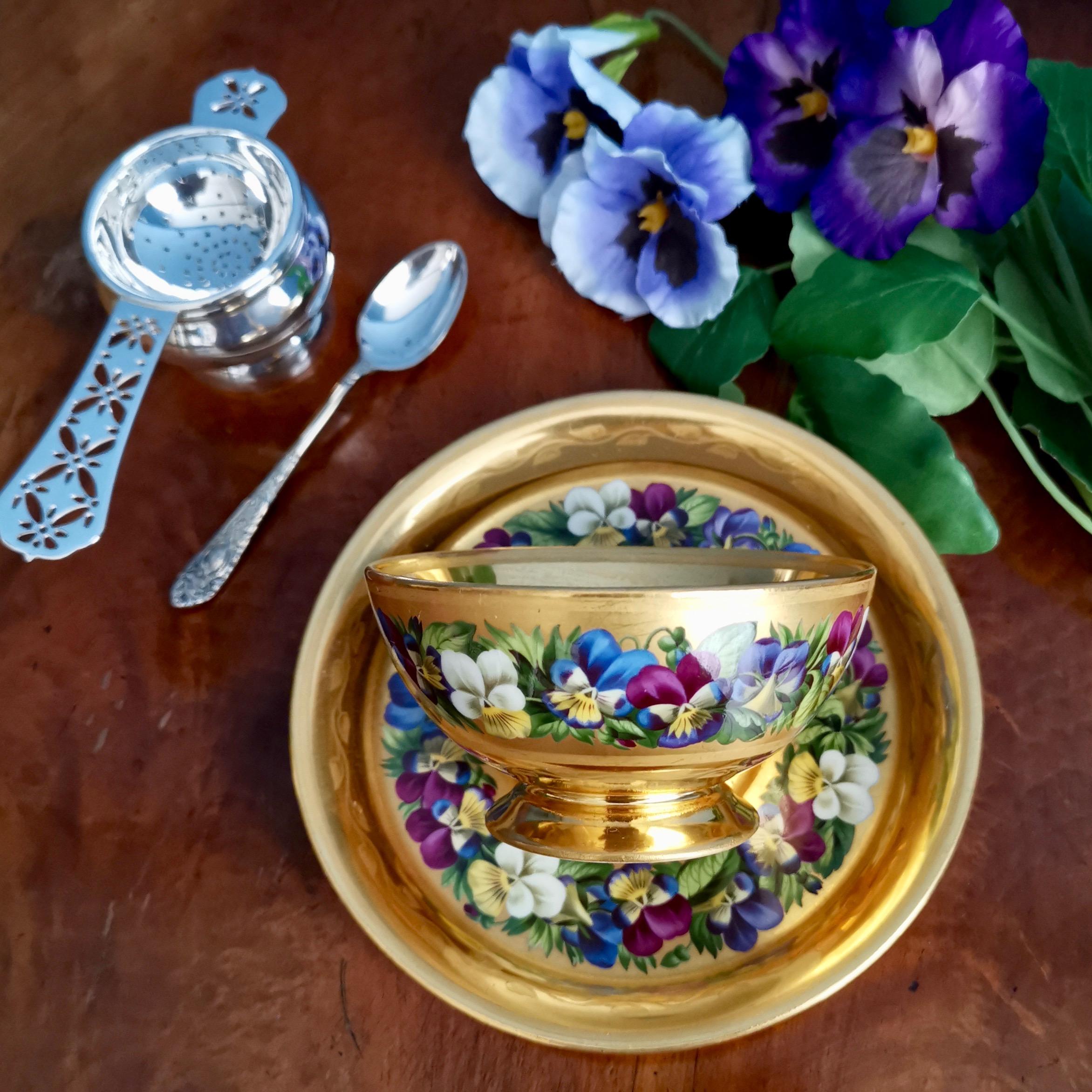 This is a beautiful teacup and saucer made by the Imperial Porcelain Factory in Vienna in 1826. The set has a lavish gilt ground and beautiful bands of pansies painted by Anton Friedl, who was famous for his flower paintings, but particularly his