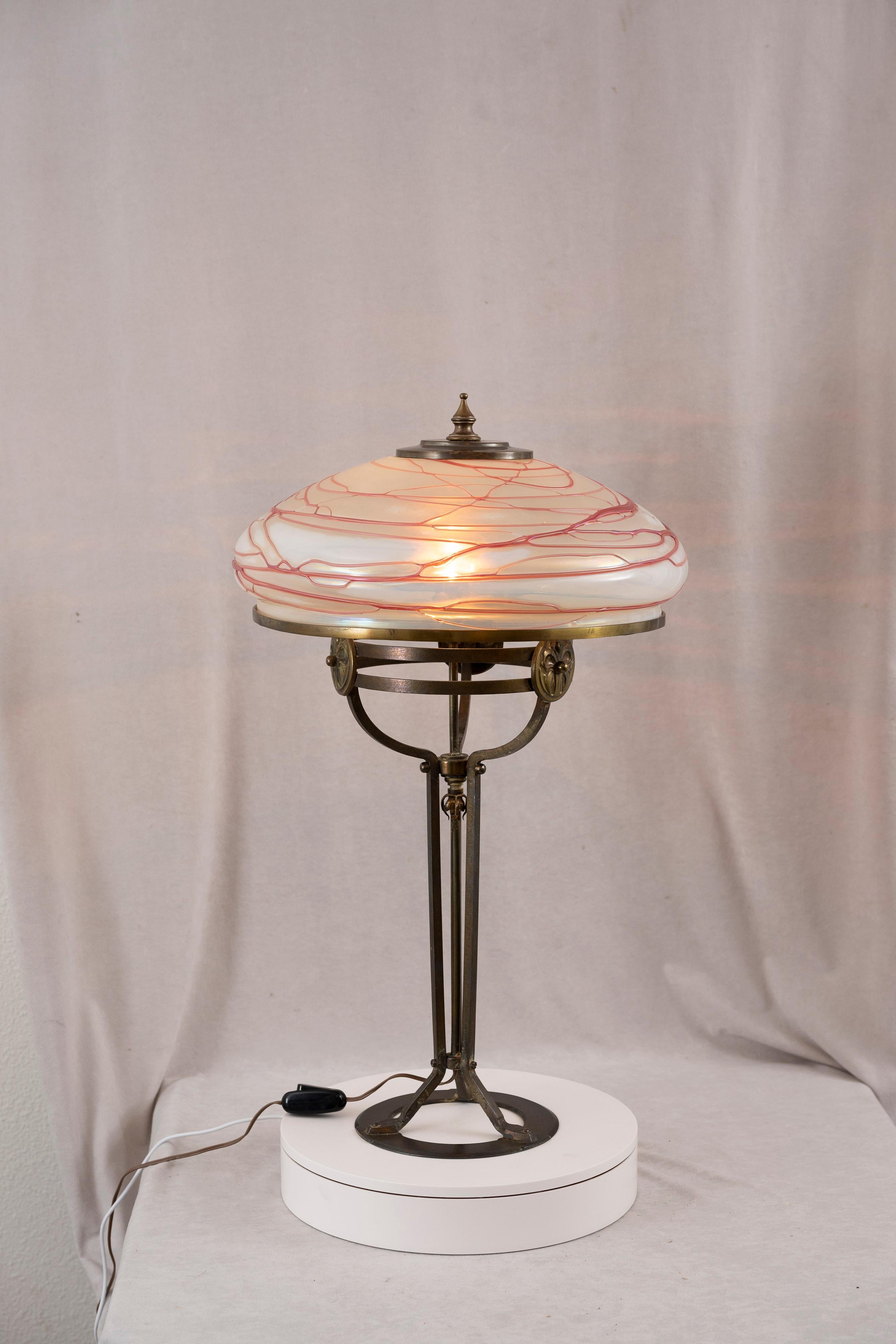  This impressive and high quality lamp was made in Austria ca.1910 and is done in the Vienna Secessionist style. This also works well with the Arts & Crafts design in one's home.
  The large hand blown shade is opalescent with glass red lacing all