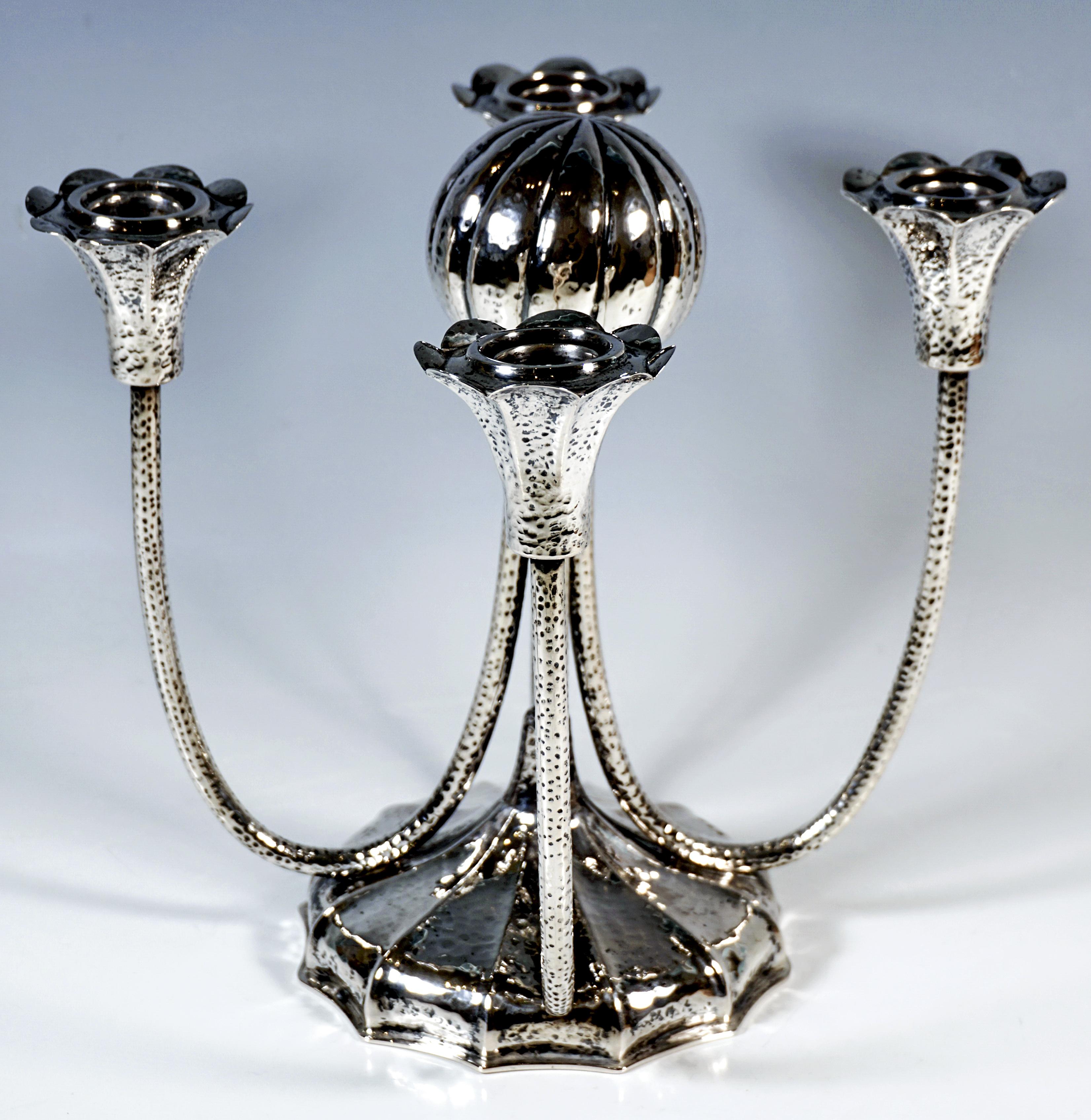 Portacandele a quattro bracci in argento martellato e cesellato, base di forma rotonda di base, bombata e nervata e segmentata in dodici raggi, appuntita al centro, con quattro sottili tubi a forma di U sulla sommità, uniti al centro da una sfera