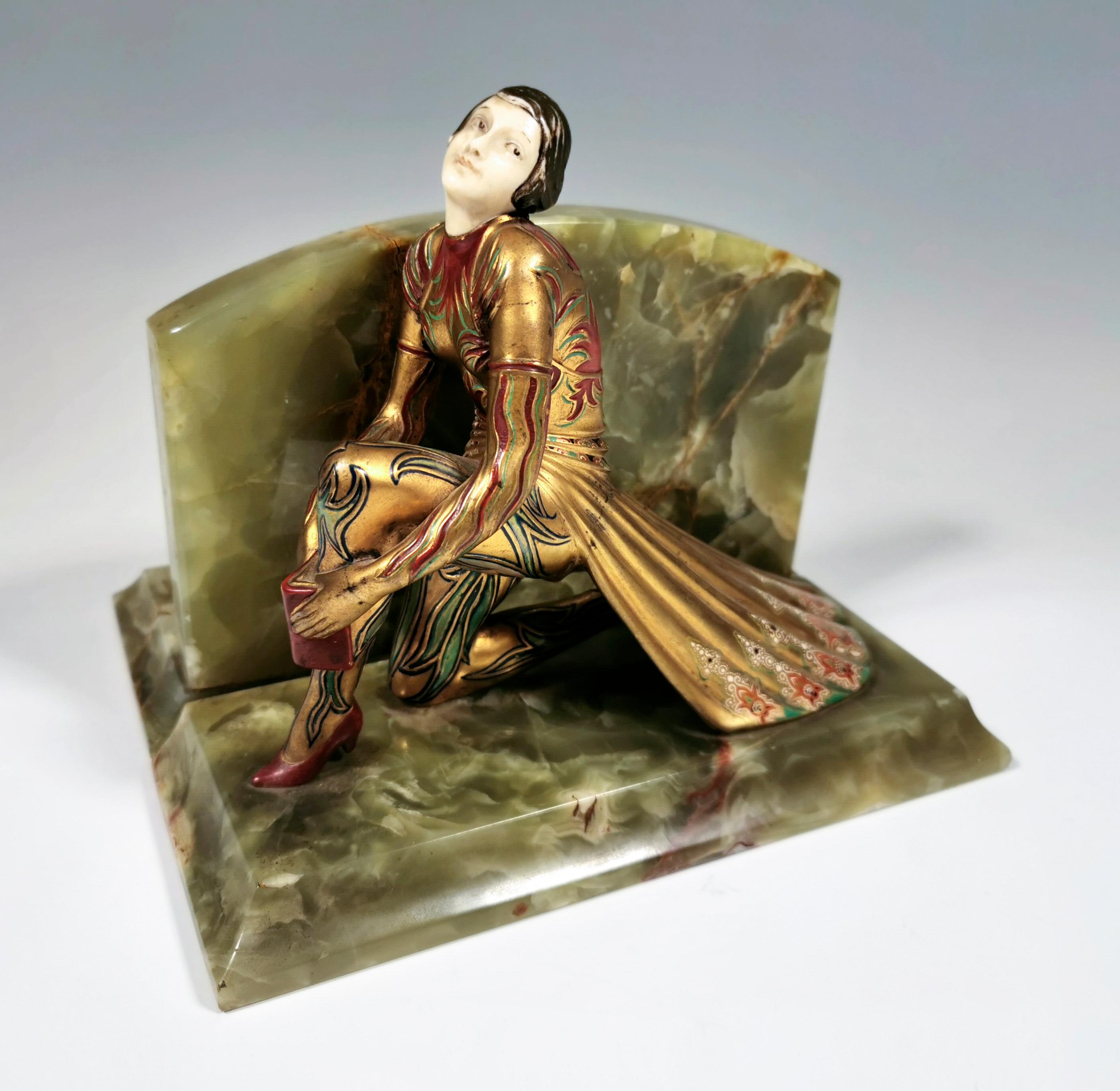 Young Art Deco dancer made of gilded and cold-painted bronze in exotic costume, kneeling on one knee, holding a book in front of the other, upright leg, looking to the side with her head made of decorated ivory. The figure is based on a rectangular
