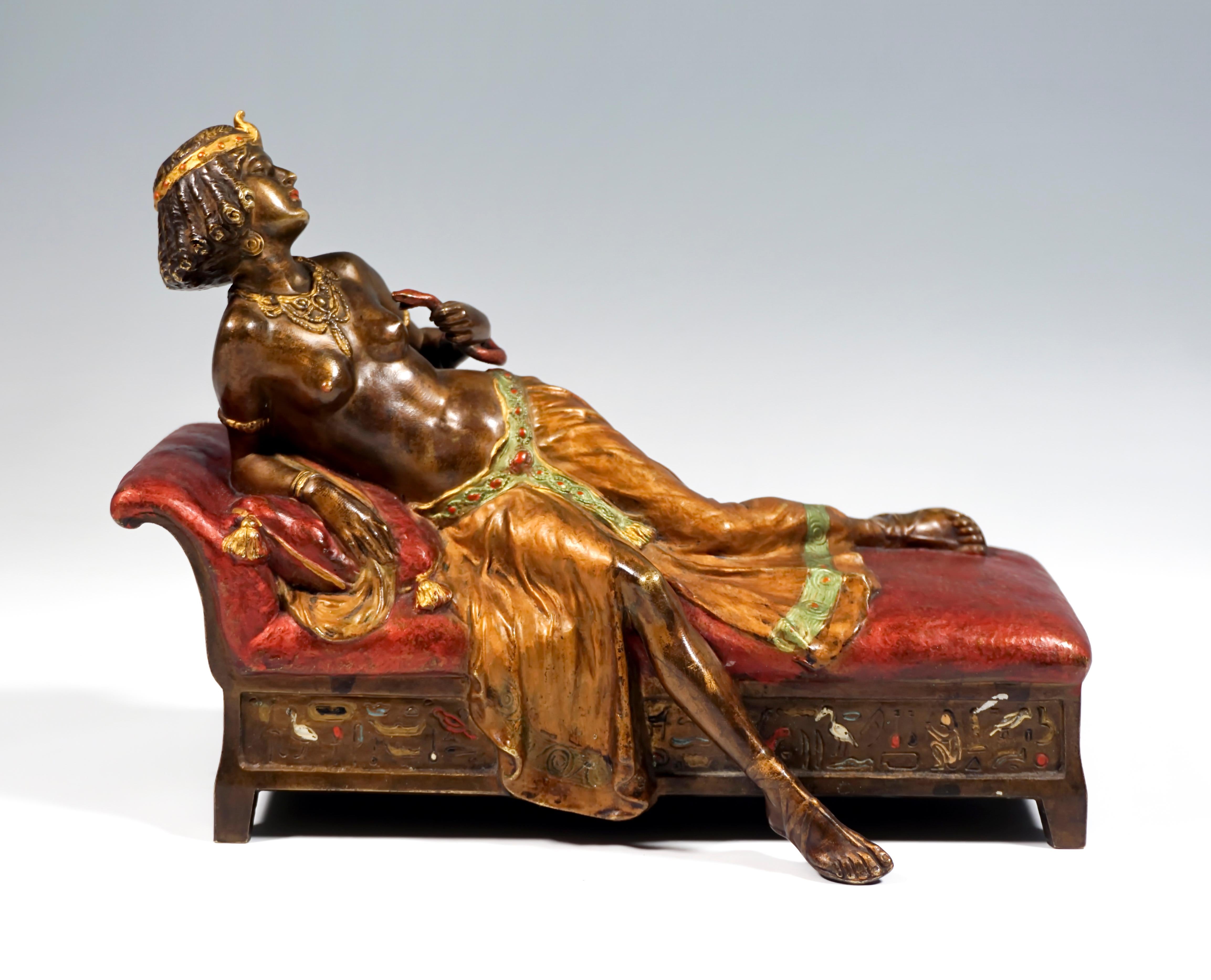 The beautiful oriental half-nude with curly hair, headdress and long, softly falling skirt lying on a chaise longue with 
hieroglyphic inscriptions and leading a snake to her chest with her left hand.
The figure is painted in color, 'Nam Greb' &