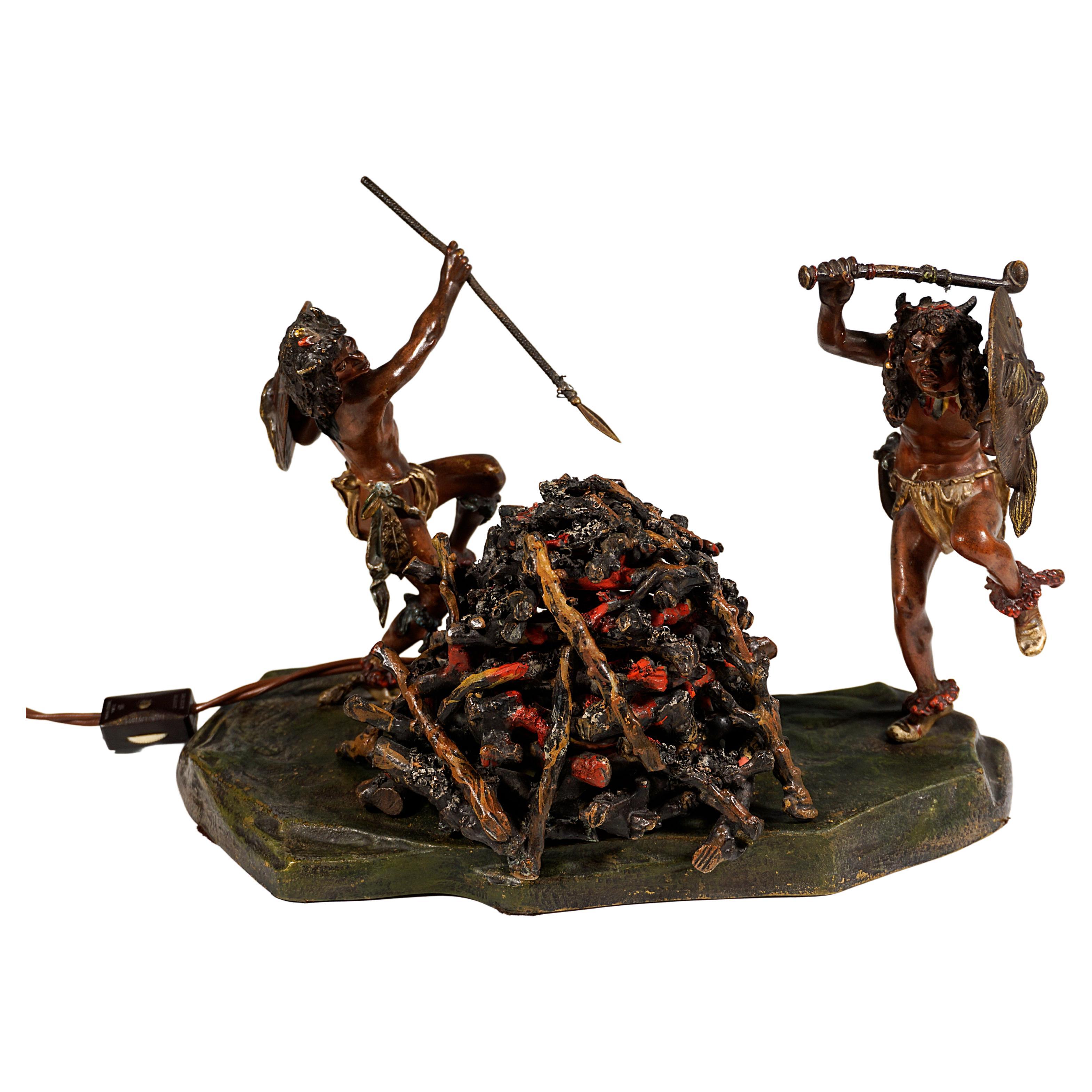 Sehr seltenes Stück Wiener Bronzekunst:
Zwei barfüßige indianische Krieger mit gehörntem Kopfschmuck und Lendentüchern sowie Federn um Hüften und Beine, mit Schilden an den Unterarmen und erhobenen Waffen, tanzen um ein Lagerfeuer.
Auf einem