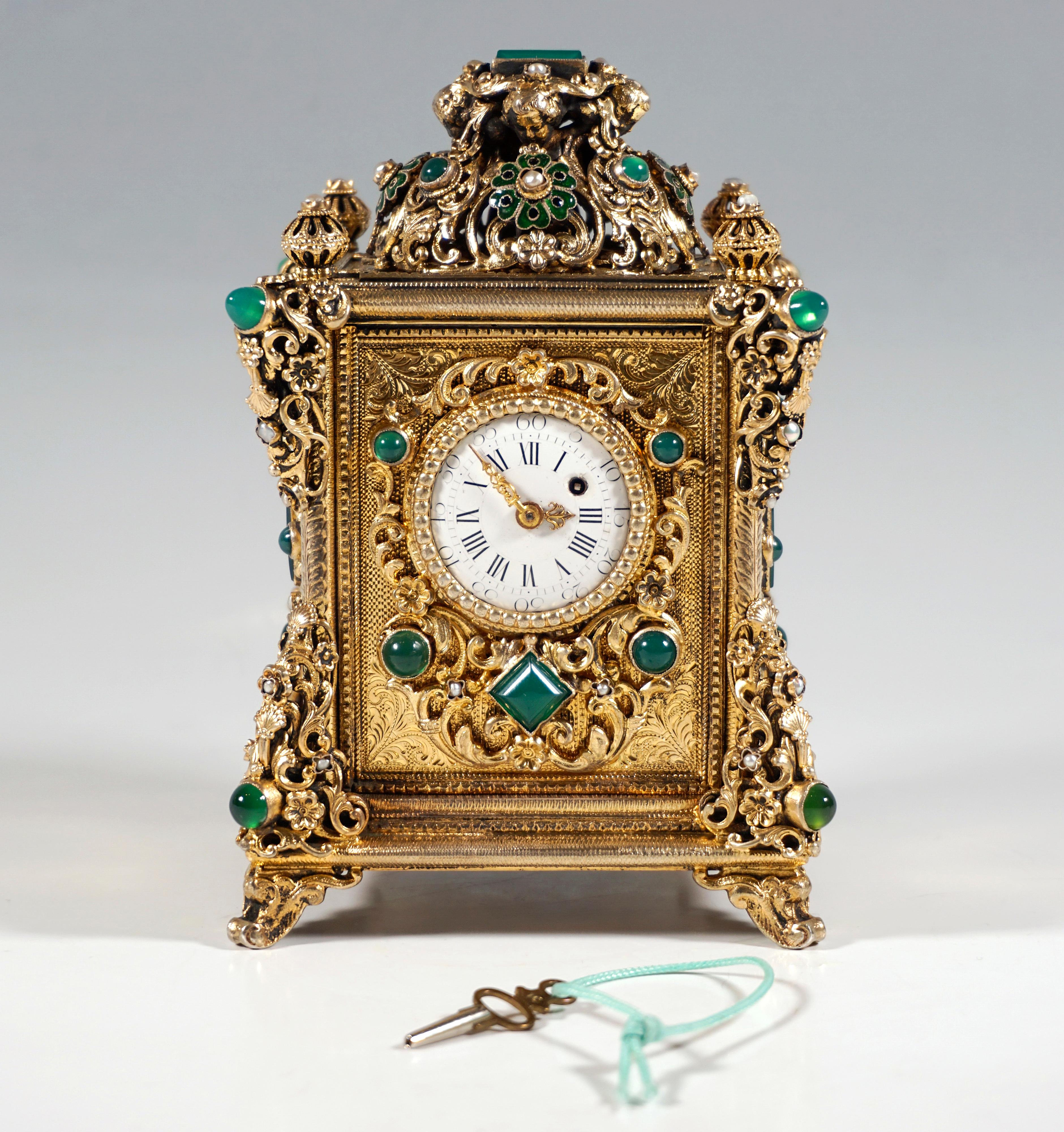 Elaborately decorated table clock in excellent condition:
Clock case in cubic basic form on four rocaille feet, all components made of silver with elaborate chasing and surface gilding, rich decoration of all surfaces, as well as corners and edges