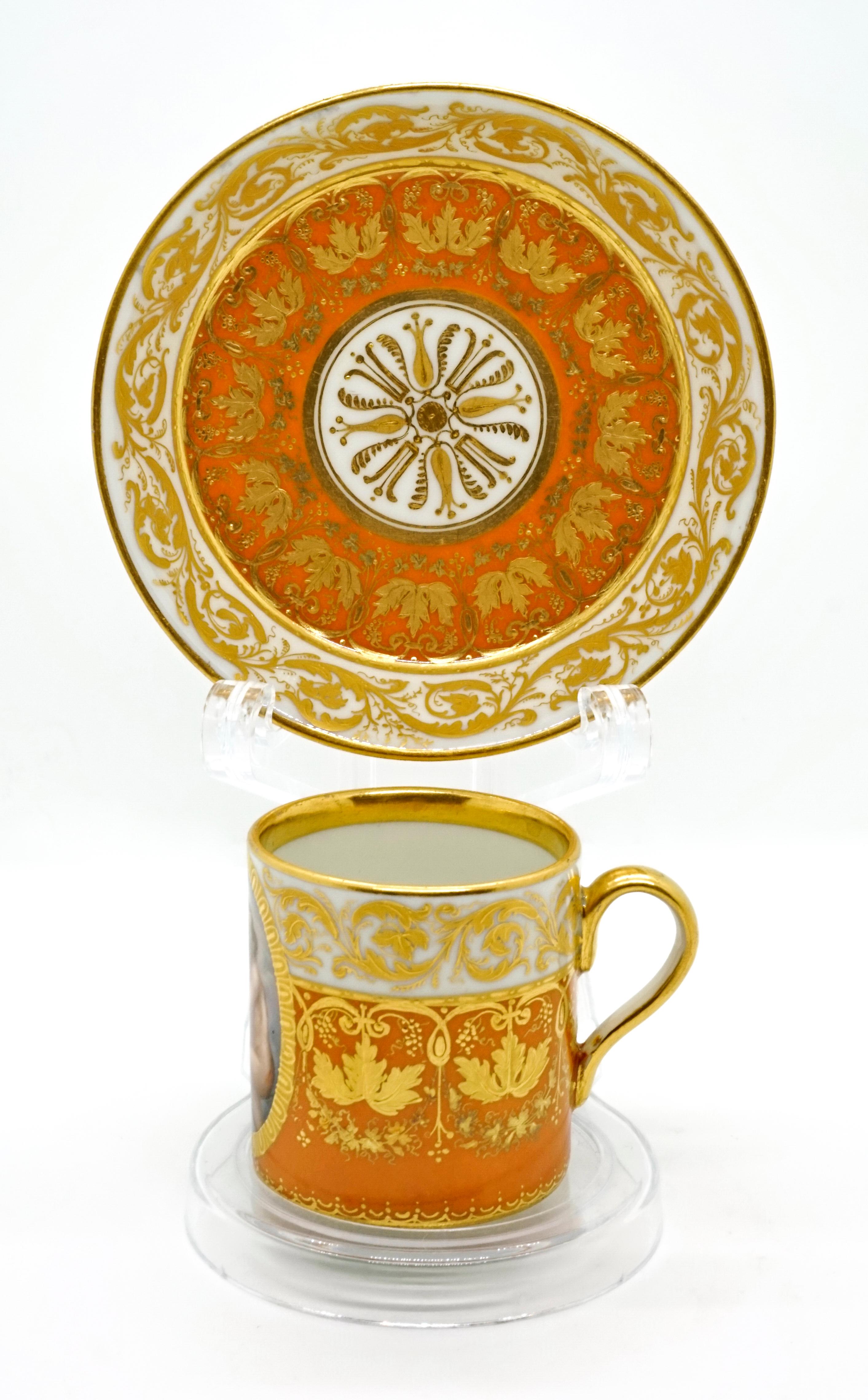 The cylindrical white cup is painted two-thirds dark yellow from the bottom upwards, and over the entire cup there is ample gold decoration with vine leaves and tendrils, gold also on the top edge and the upper inner rim. Opposite the curved handle